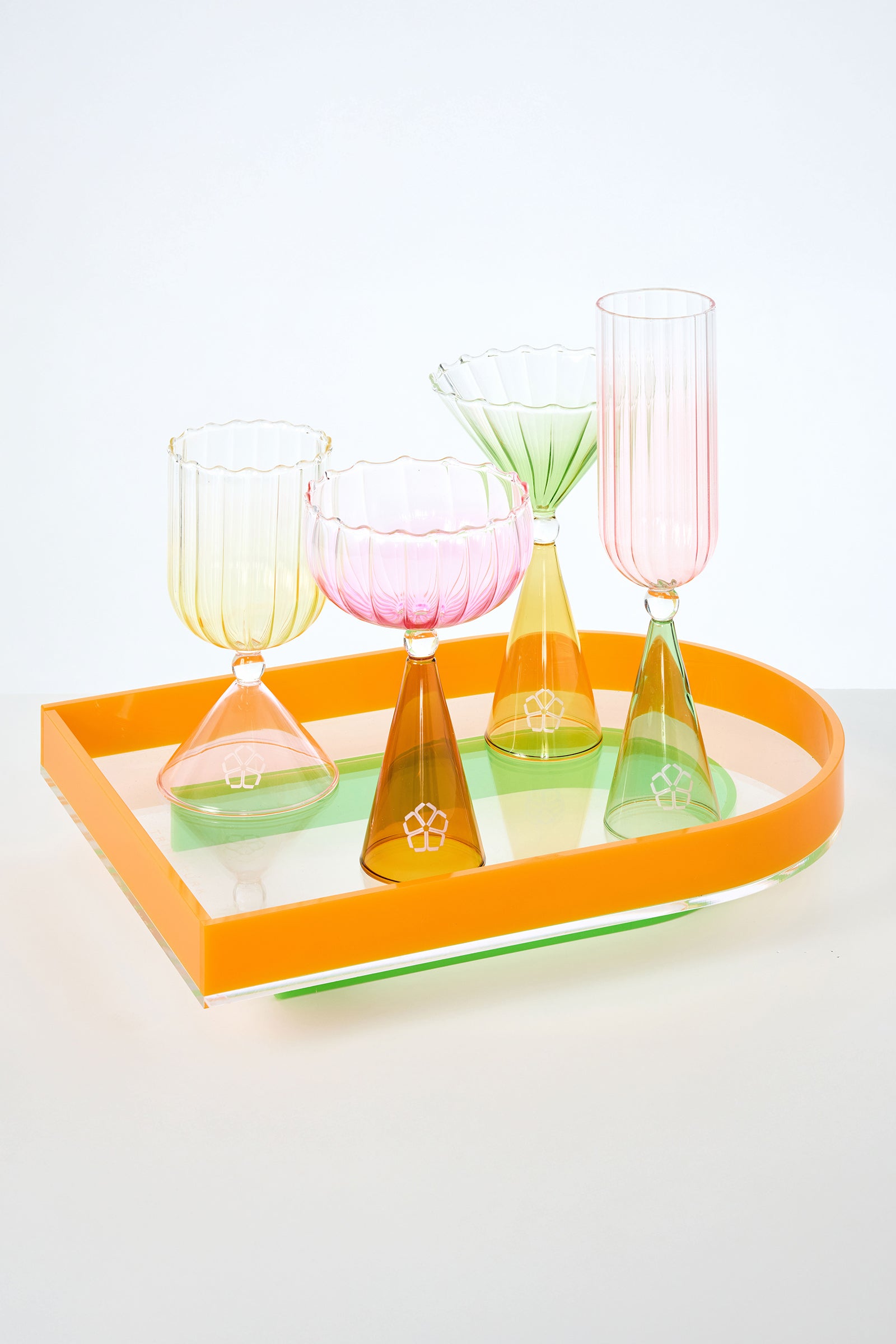 The Cocktail Glass Set with Silicone Floret Mold features four uniquely shaped, multi-colored glass cups with geometric stems, displayed in a bright orange tray against a white background.