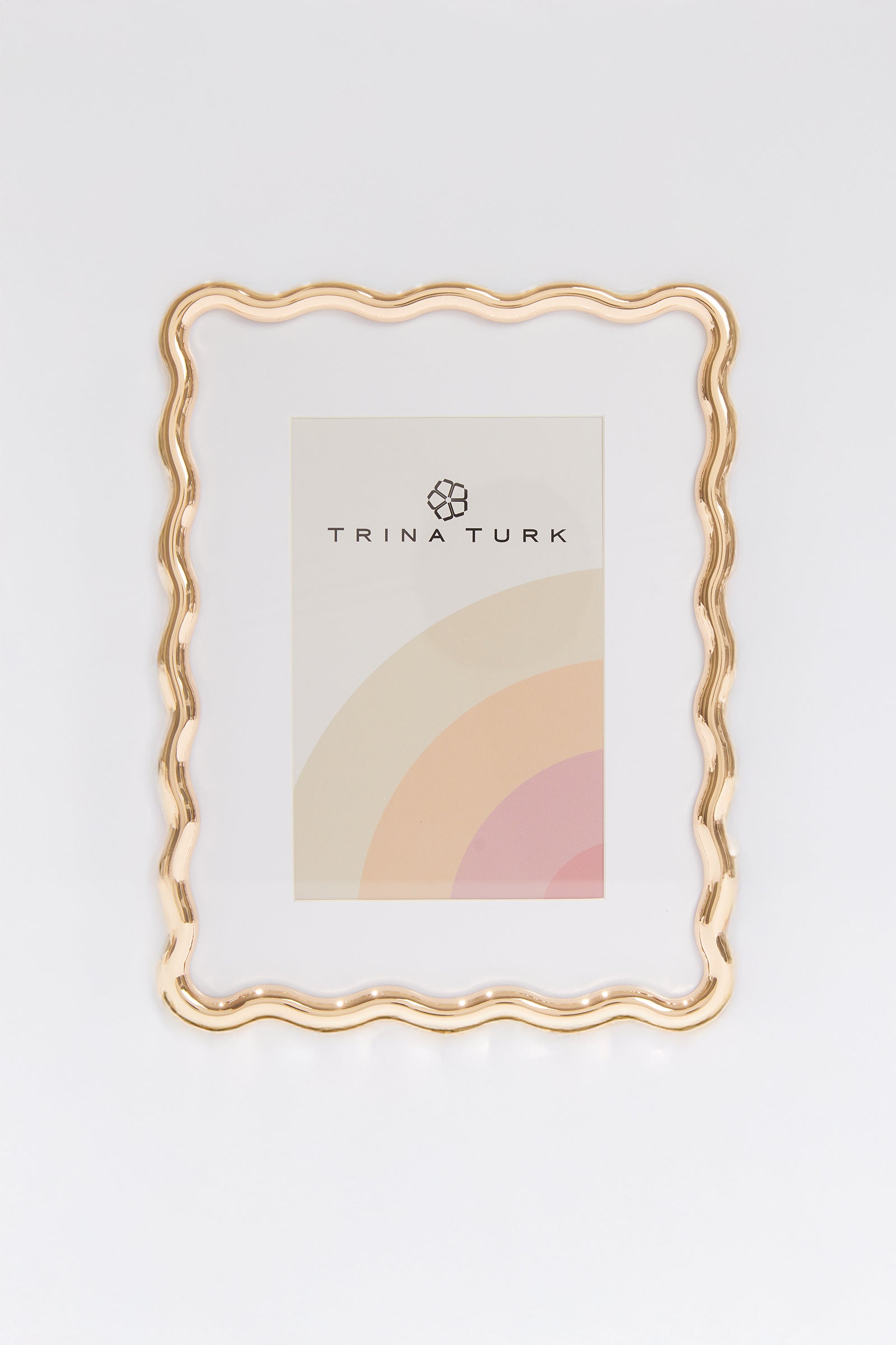 The Trina Turk Wavy Gold Picture Frame in MULTI features pastel rainbow arcs and a geometric logo beside the brand text on white, making it a stylish 4x6 frame for showcasing your favorite memories.