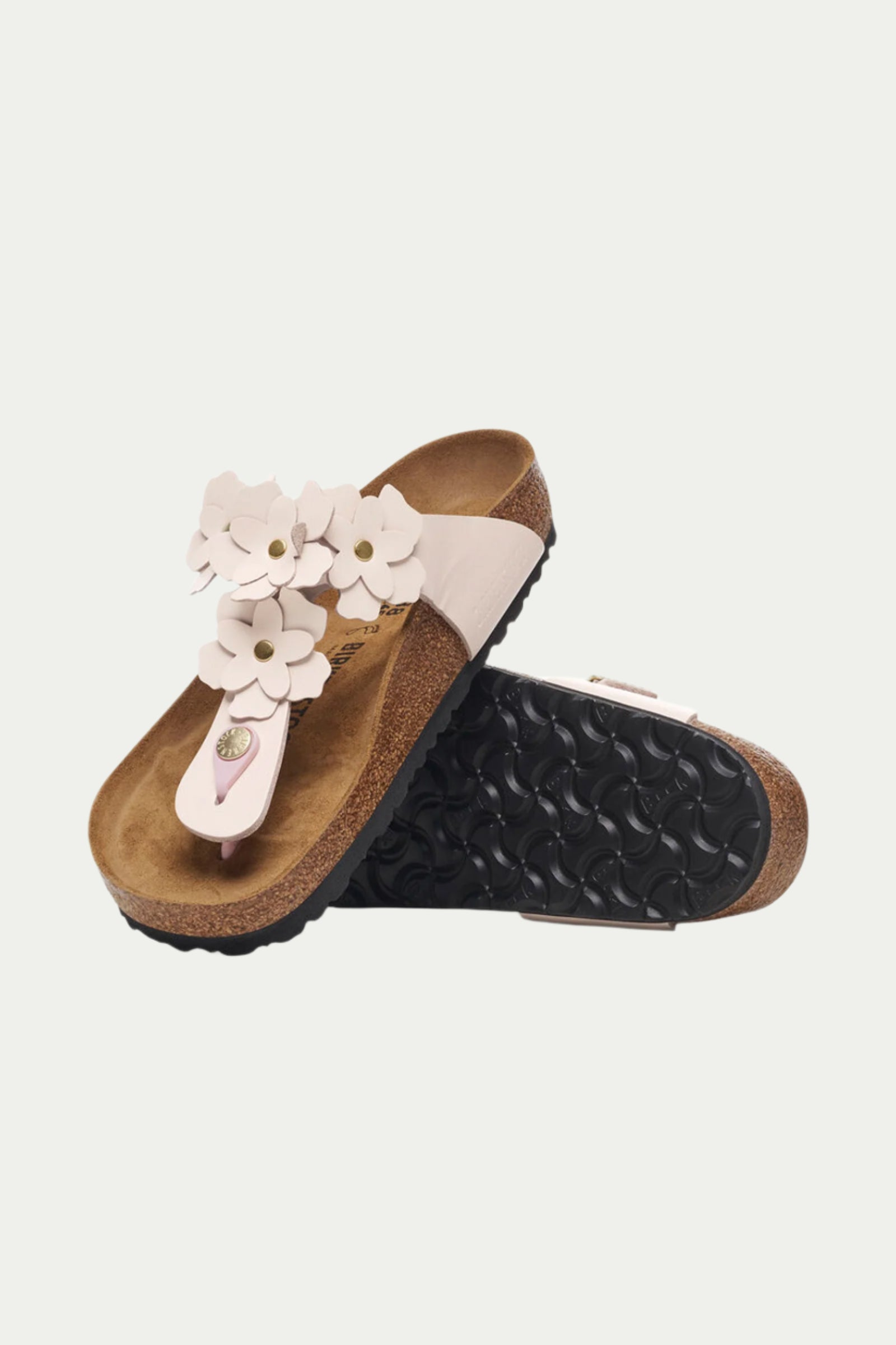 The Womens Gizeh Flowers Leather Sandal - Rose features cork soles, light pink straps, and decorative white flowers, displayed with one sandal upright and the other showing its black textured sole.