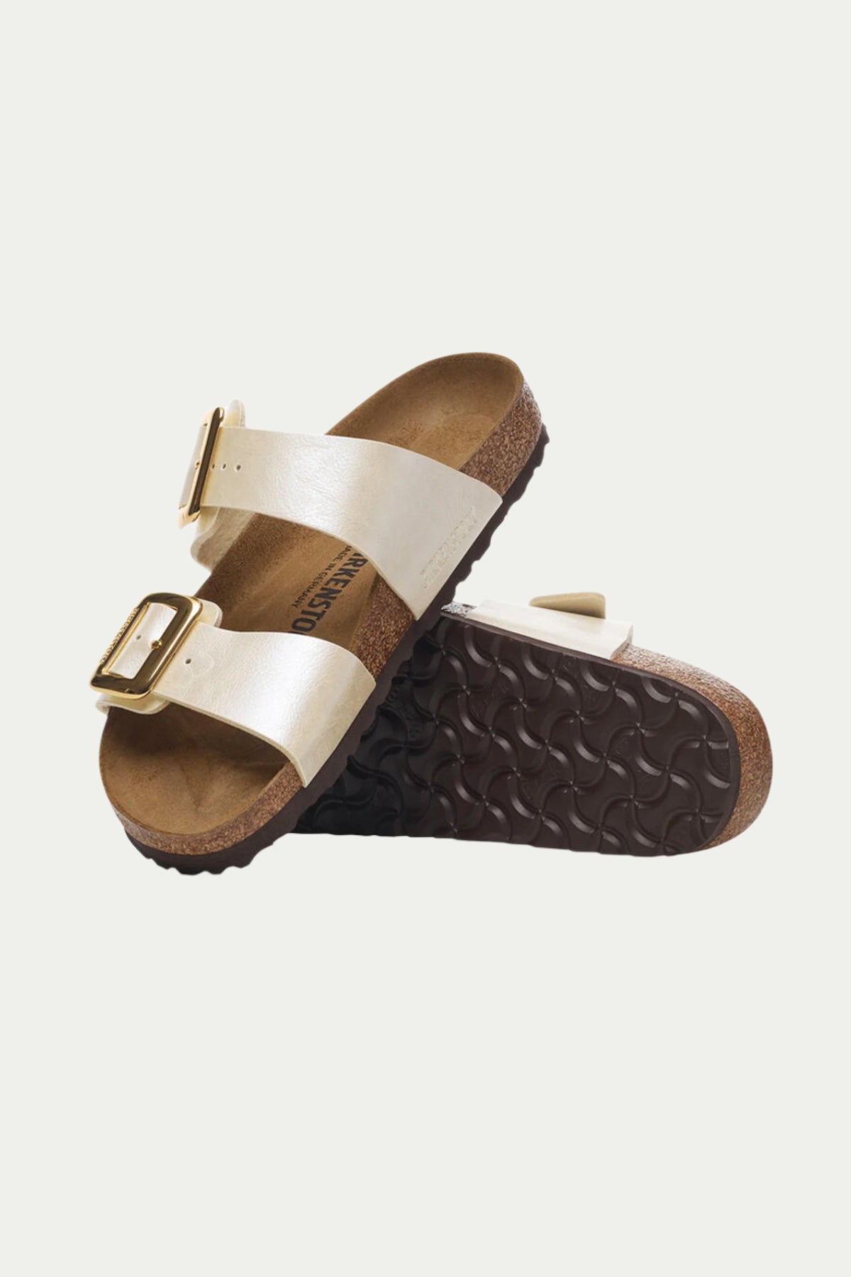 The Womens Sydney Luxe Buckle Sandal in beige features two straps with gold buckles; one sandal stands upright, revealing its cork footbed, while the other shows the textured brown sole.