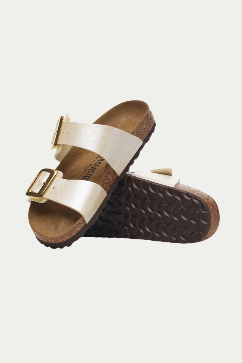 The Womens Sydney Luxe Buckle Sandal in beige features two straps with gold buckles; one sandal stands upright, revealing its cork footbed, while the other shows the textured brown sole.