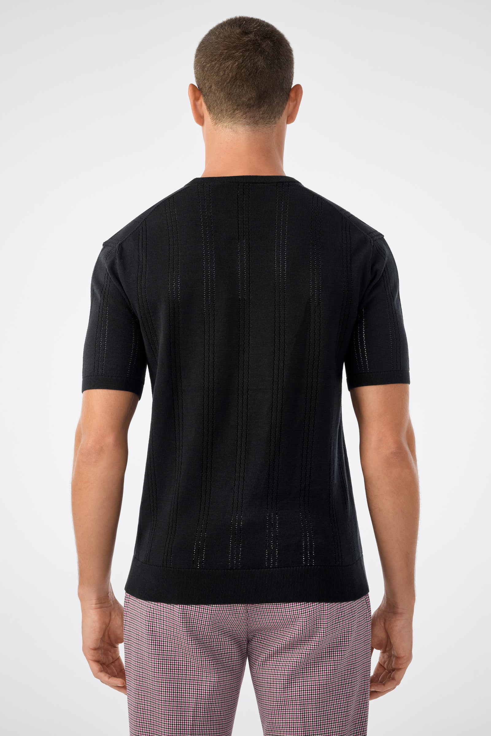 A man with short hair is shown from behind, wearing the Carlo Ss Crewneck in black and light pink checkered pants against a plain light gray background.