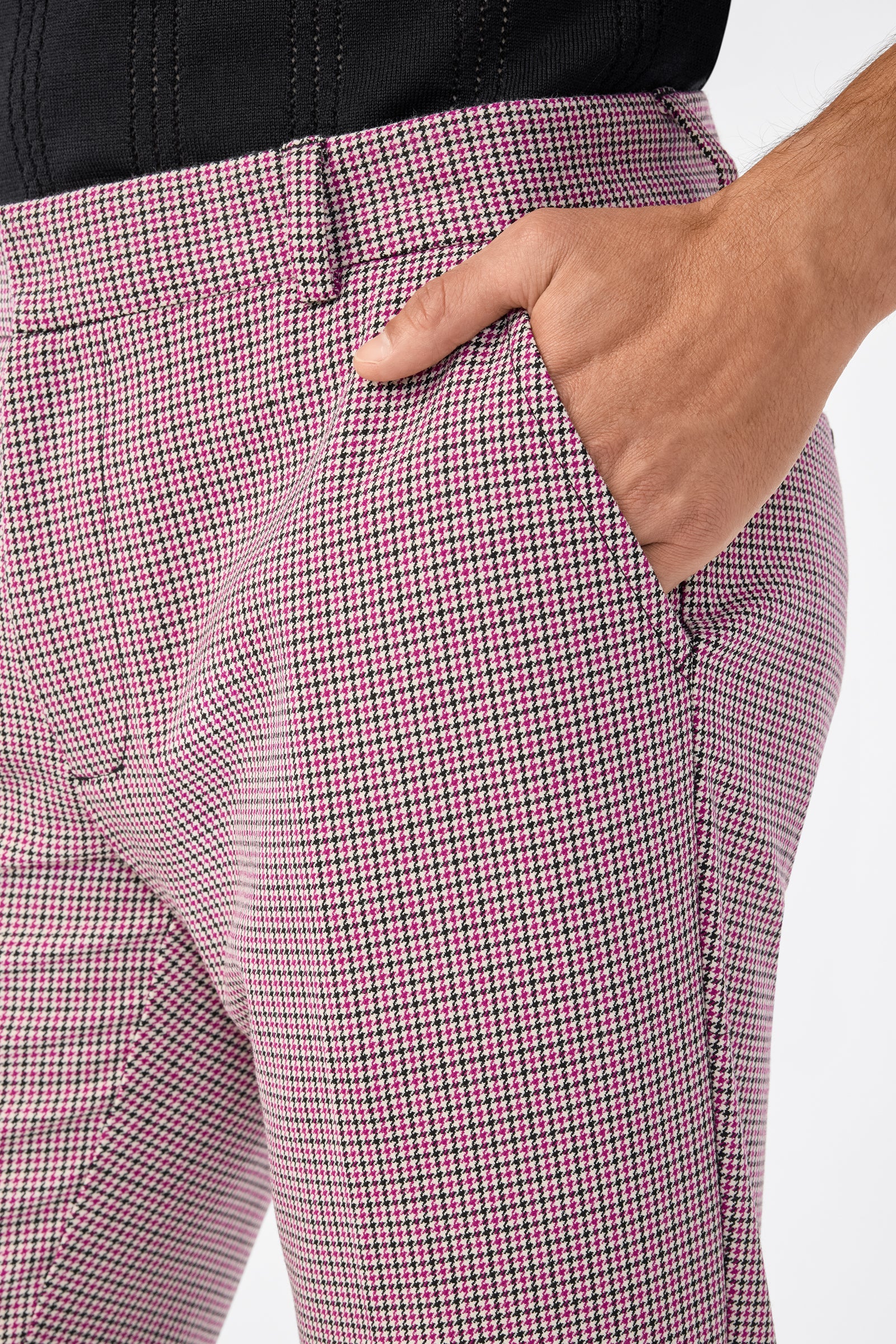 Close-up of a person wearing the Clyde Slim Trouser in pink and black houndstooth with their right hand in the front pocket, paired with a black top.
