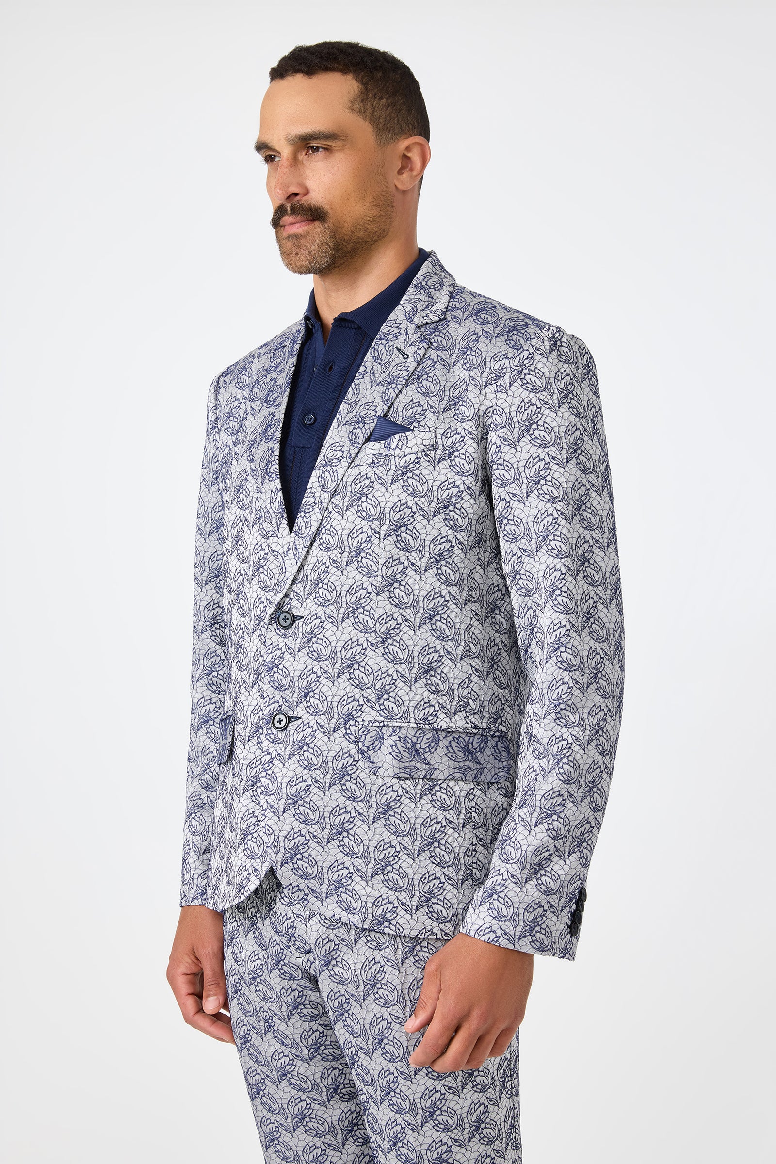 A man wearing the Thurston Blazer - Efflorescent Jacquard, a patterned light blue and white suit jacket with a dark blue dress shirt, stands against a plain white background, looking slightly to the side.