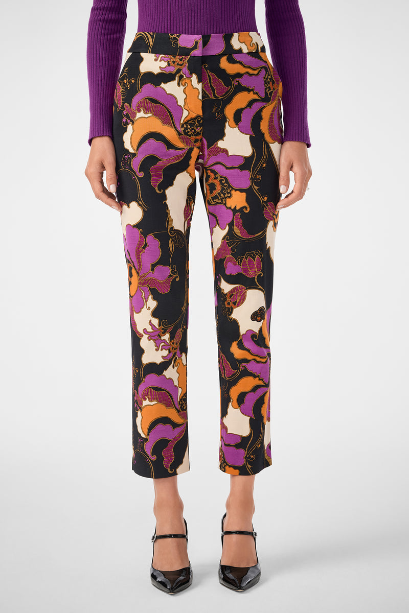 Someone wearing the Moss 2 Pant—high-waisted, straight-leg pants with a bold purple, pink, orange, and black floral pattern—paired with a purple ribbed sweater and black pointed-toe heels.