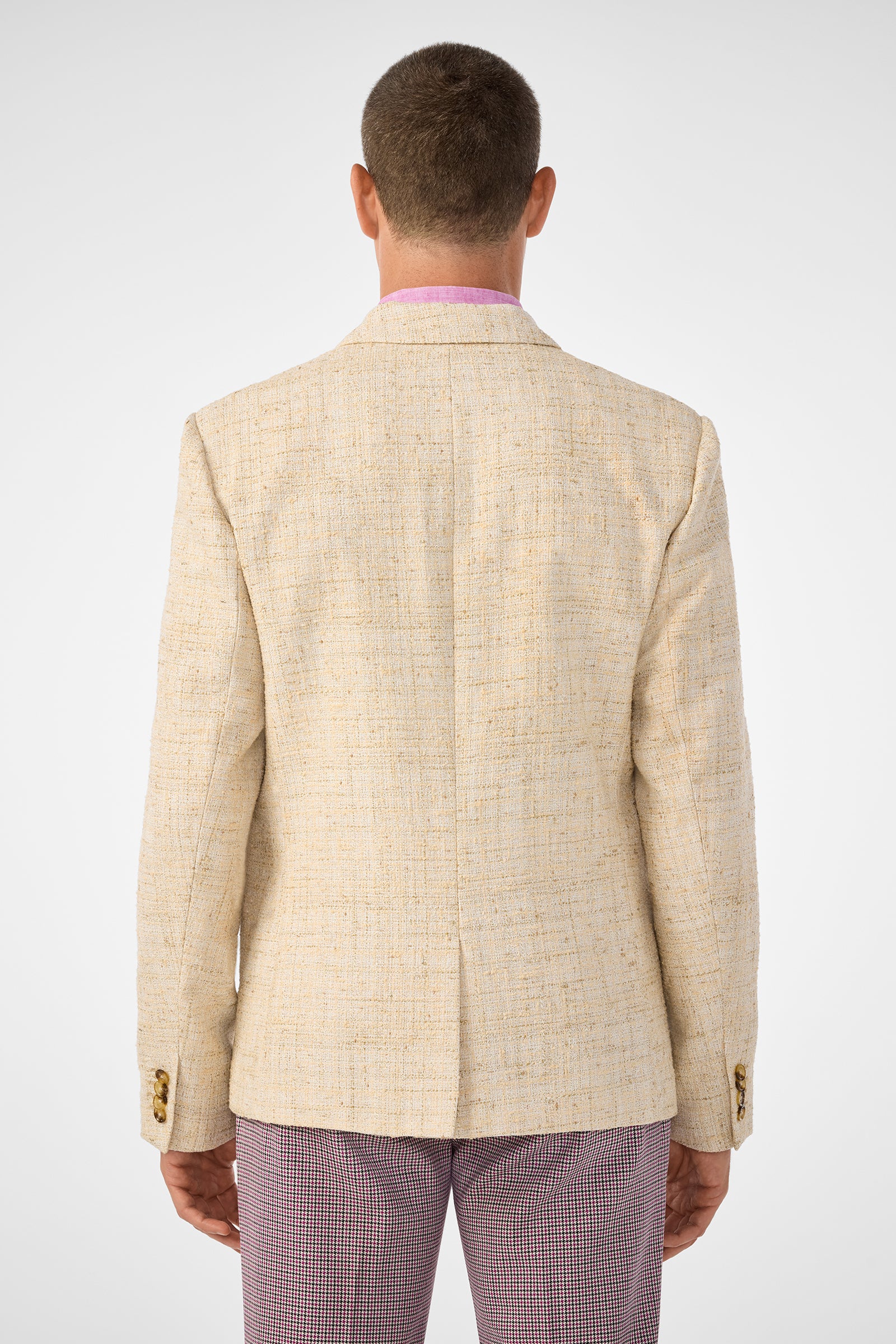 A person with short hair is shown from behind, wearing the beige textured Thurston Blazer with gold buttons and pink checkered pants against a plain light background.