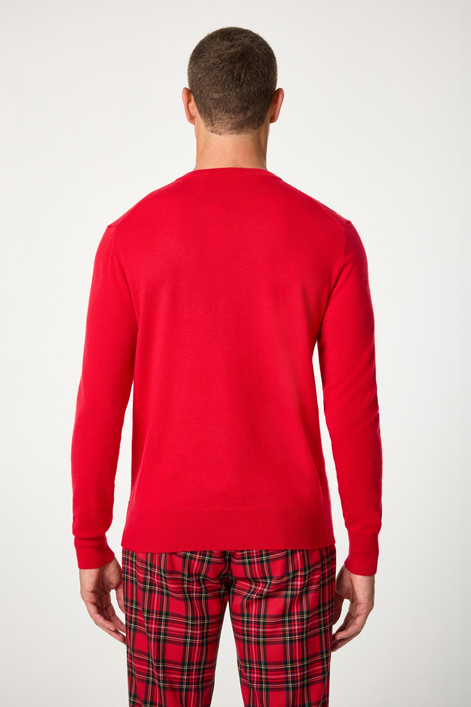 A man faces away from the camera, wearing the Lover V-Neck Sweater in bright red, paired with red plaid pants, set against a plain white background.