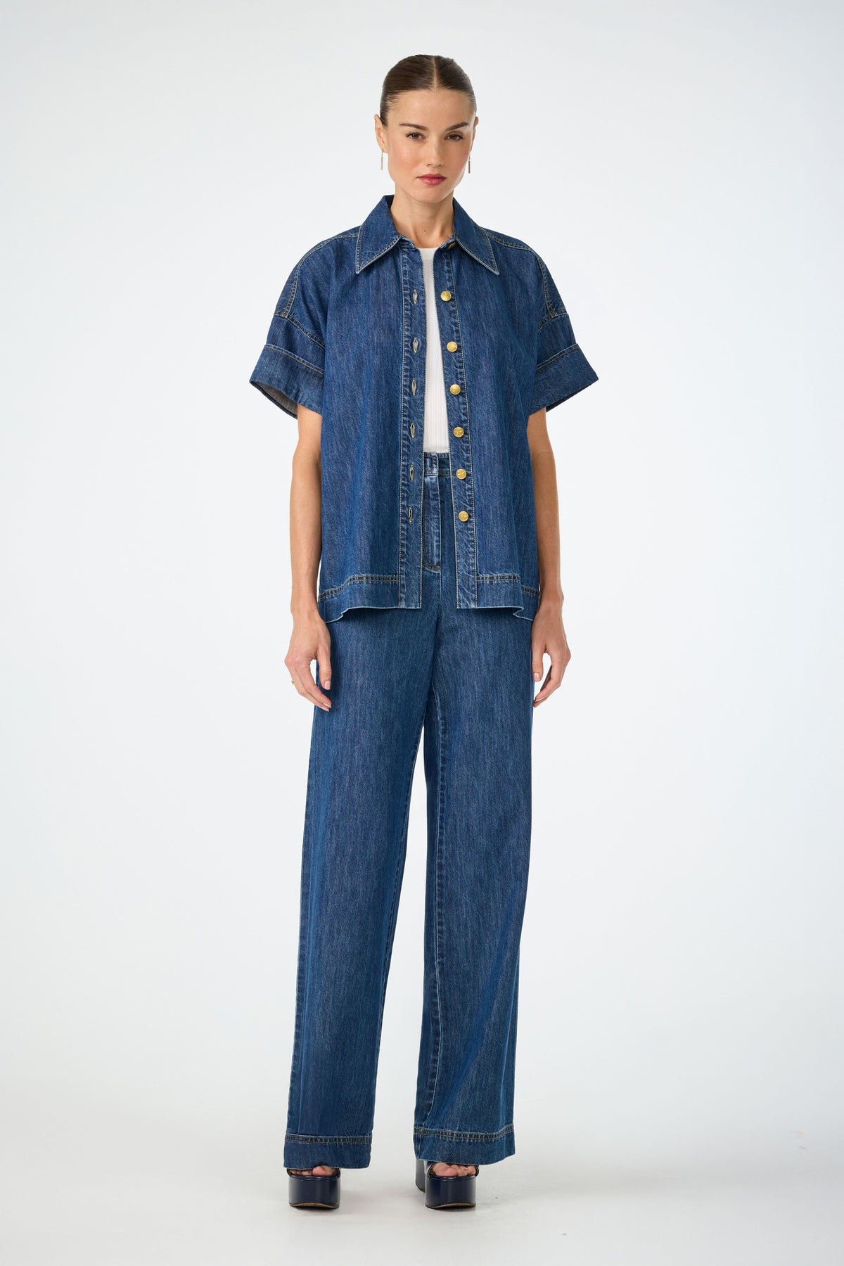 A woman faces forward wearing the Opponent 2 Short-Sleeve Top over a white top, paired with matching high-waisted wide-leg denim pants and black platform sandals, against a plain white background.
