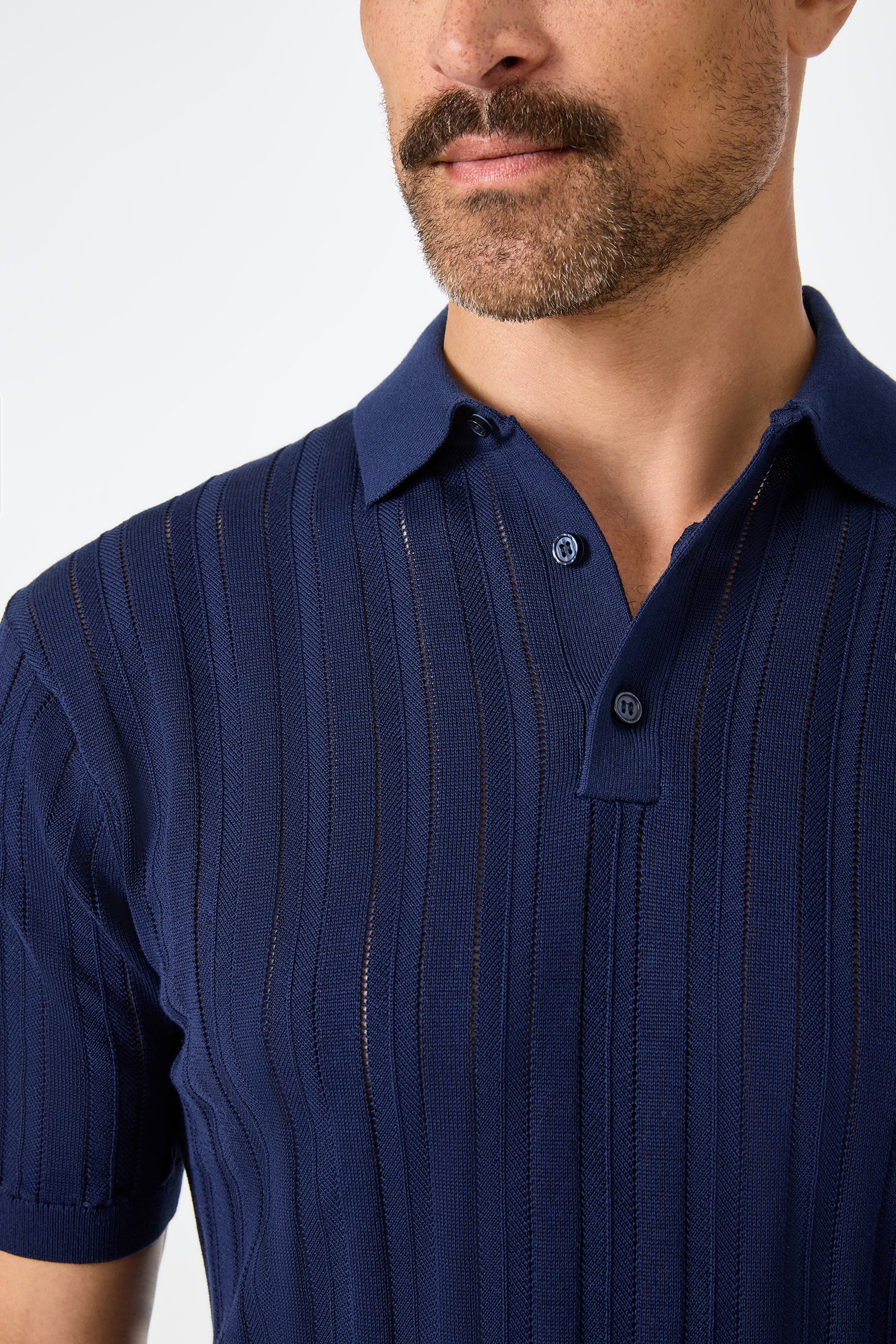 A man with a mustache wears the Kensington Short-Sleeve Polo—a navy blue, ribbed, semi-sheer knit shirt with a collar—photographed from the chest up against a plain background.