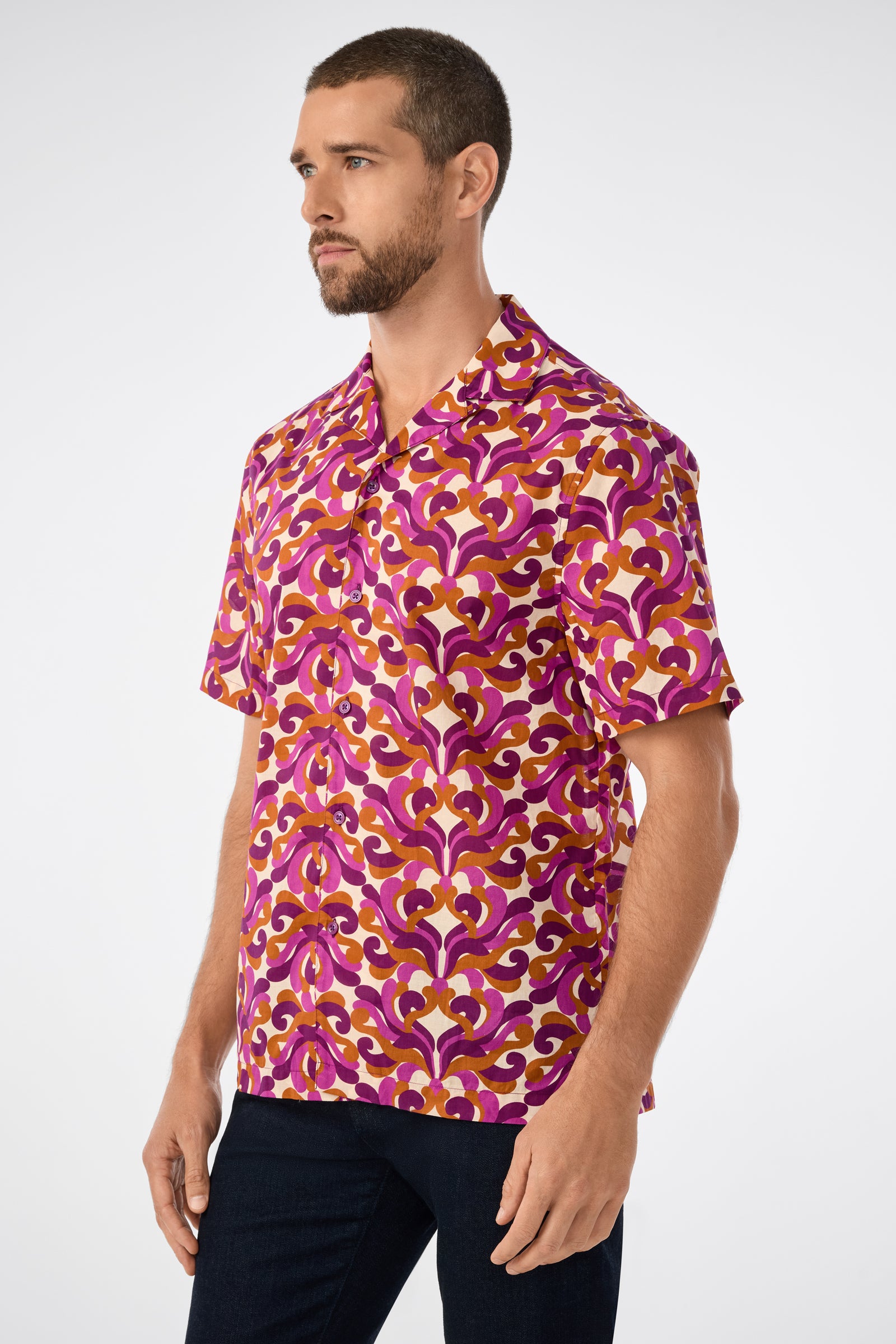 A man with short brown hair and a beard wears the Felix Ss Camp Shirt, a short-sleeved button-up with a bold pink, purple, and yellow geometric pattern, standing against a plain white background.