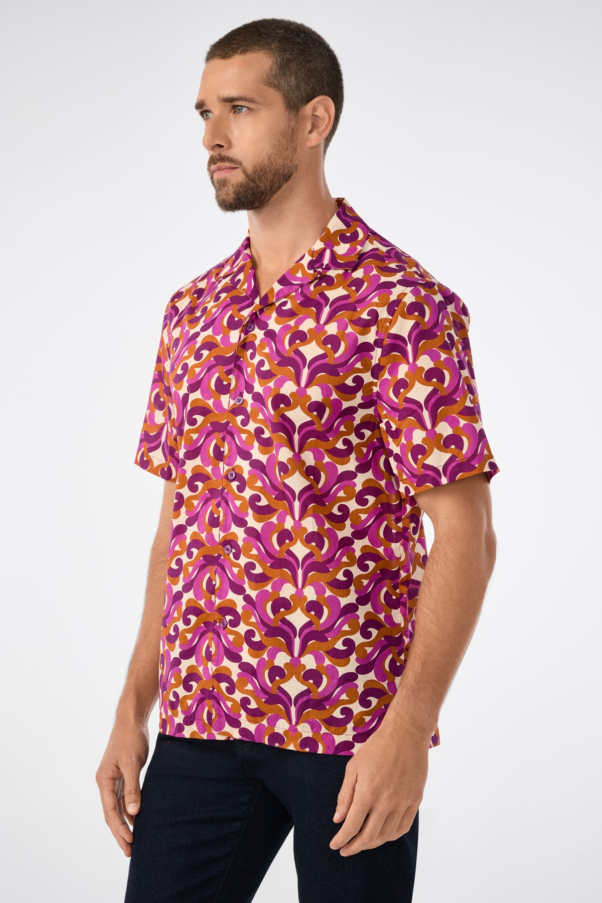 A man with short brown hair and a beard wears the Felix Ss Camp Shirt, a short-sleeved button-up with a bold pink, purple, and yellow geometric pattern, standing against a plain white background.