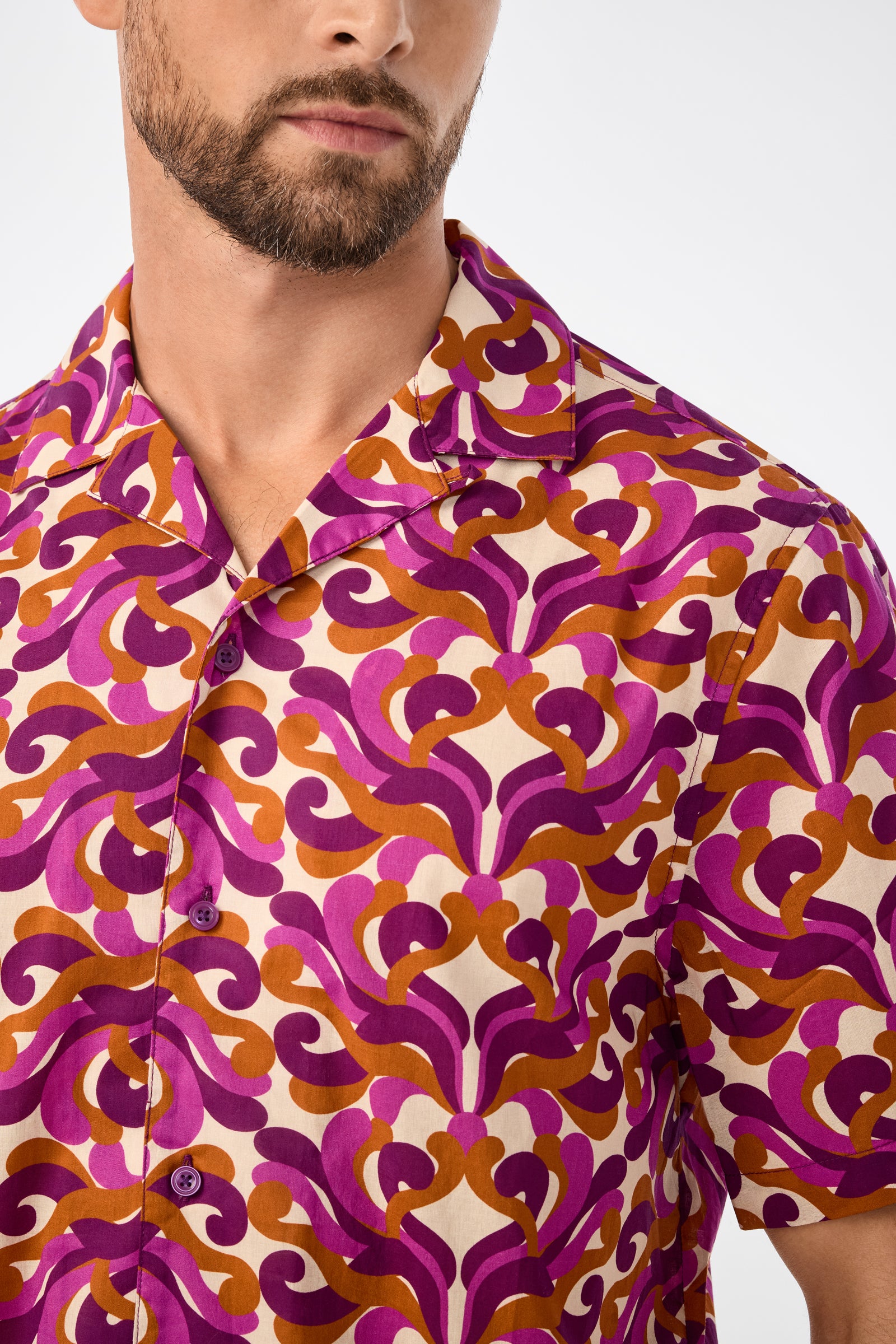 A man with a beard wears the Felix Ss Camp Shirt, a short-sleeve button-up with a bold, colorful magenta, orange, and cream pattern. The photo is cropped to show his upper torso and part of his face.