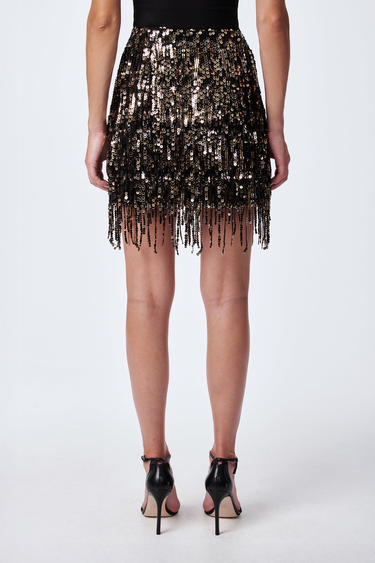 A person wearing the Rico Sequin Fringe Skirt and black high-heeled sandals is shown from the back against a plain white background.