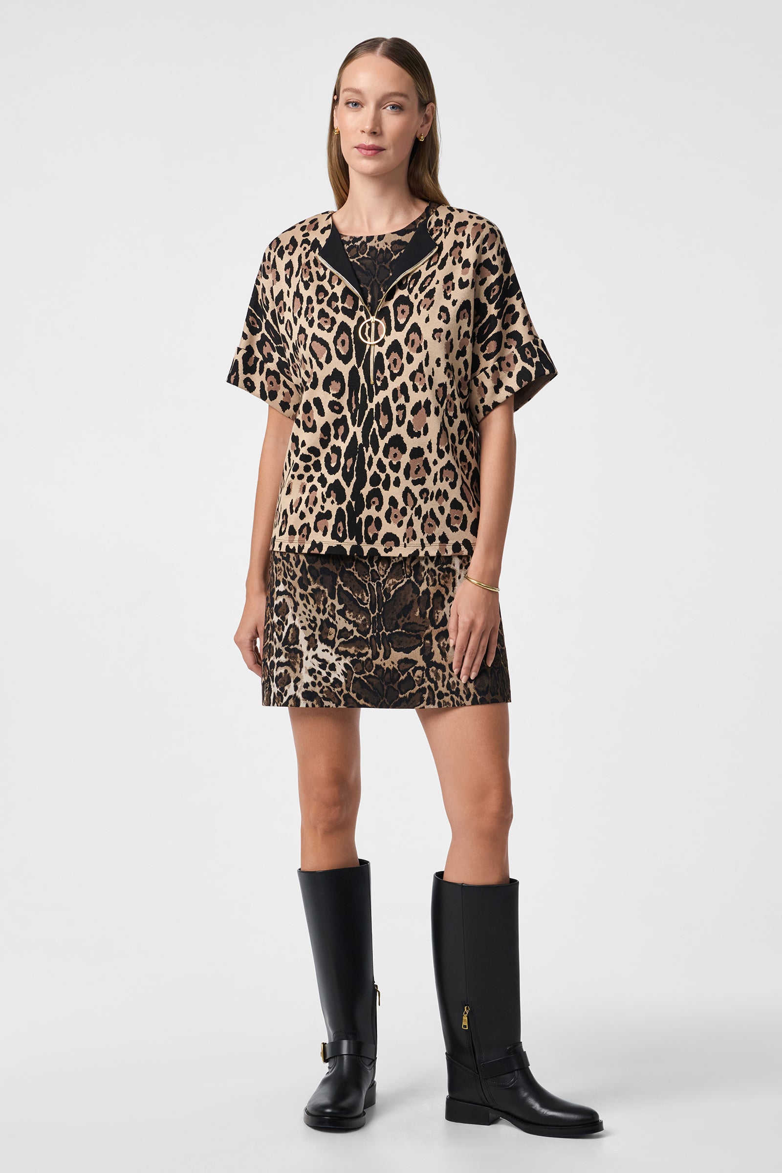 A woman faces forward wearing the Stagehands Top, a short-sleeved leopard print shirt paired with a matching skirt and knee-high black zip-up boots. She has straight light brown hair and a neutral expression.