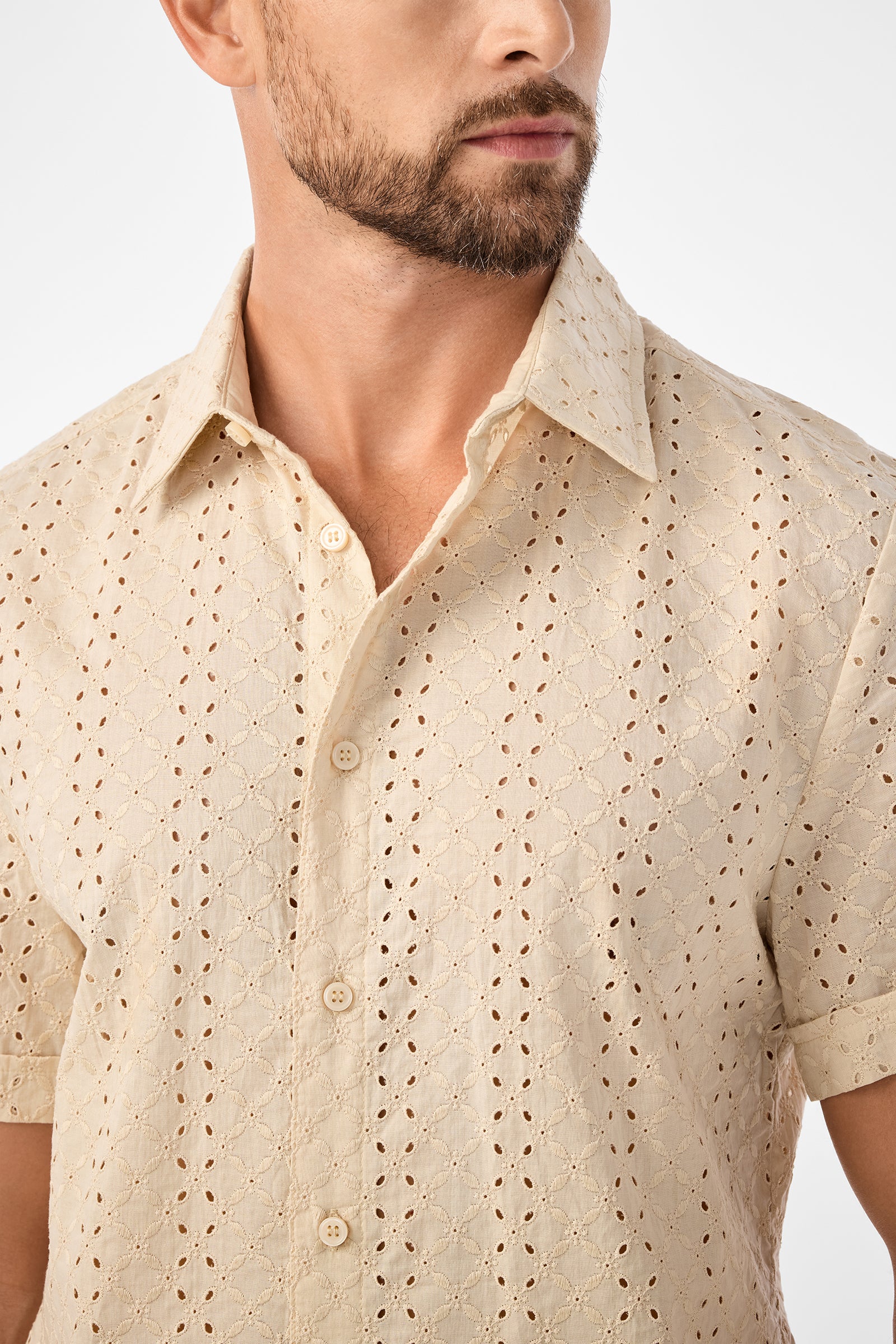 A man with a short beard, partially visible, wears the Branson Shirt—a light beige, short-sleeve button-up with an eyelet pattern and small diamond-shaped cutouts in the textured fabric.