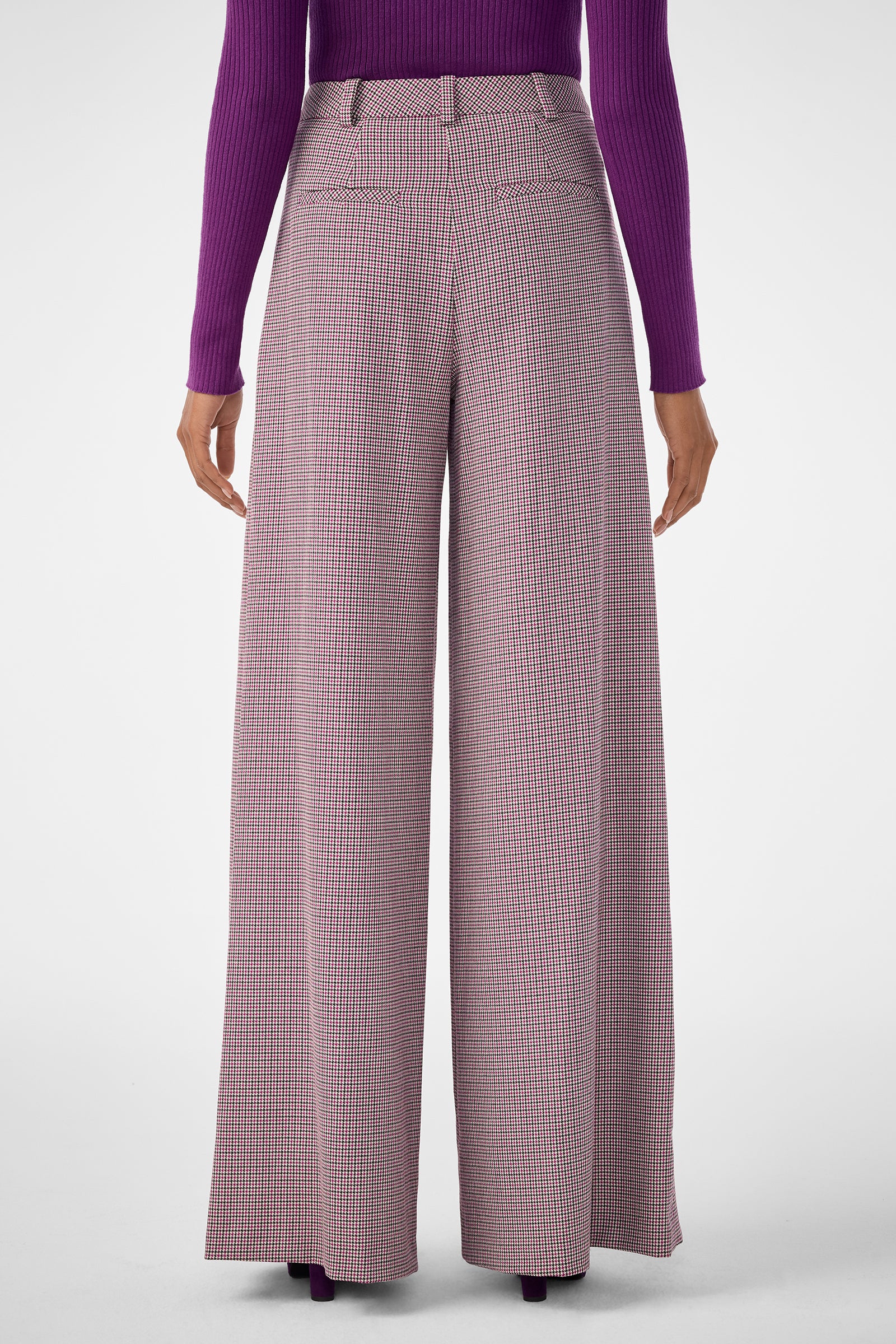 A person wearing the Solani Pant, featuring wide-leg, high-waisted plaid design, paired with a long-sleeved purple ribbed top and shown from the back against a plain light background.