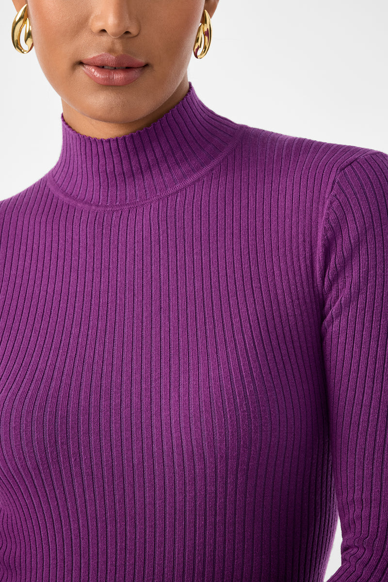 A woman wears gold hoop earrings and a purple, ribbed, long-sleeve Hempstead Sweater with a mock neck. Only her lower face, neck, and upper torso appear against a plain white background.