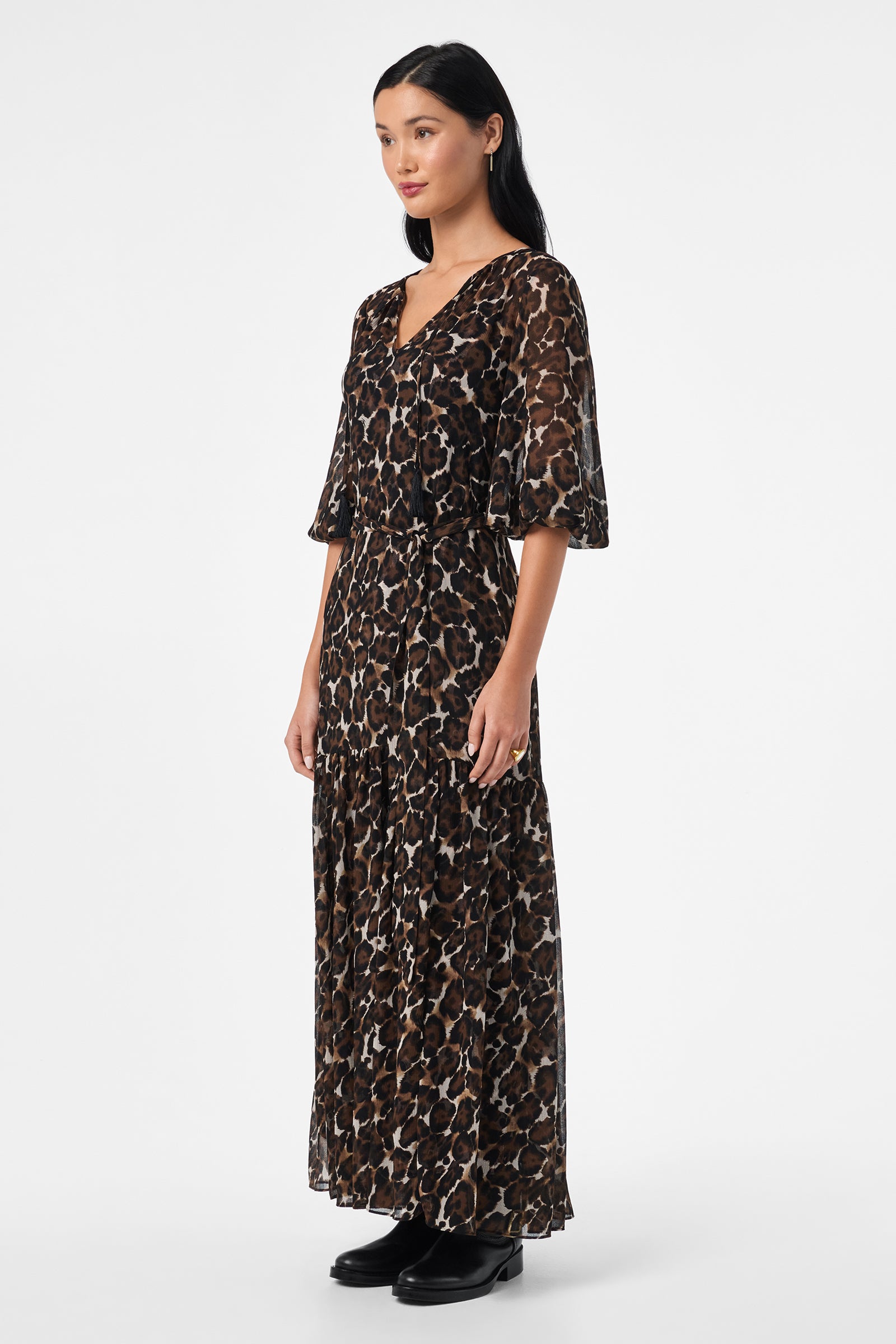 A woman wears the Shalina Tie-Waist Maxi Dress, featuring a long, loose fit with a brown and black leopard print, short wide sleeves, and black ankle boots against a plain white background.