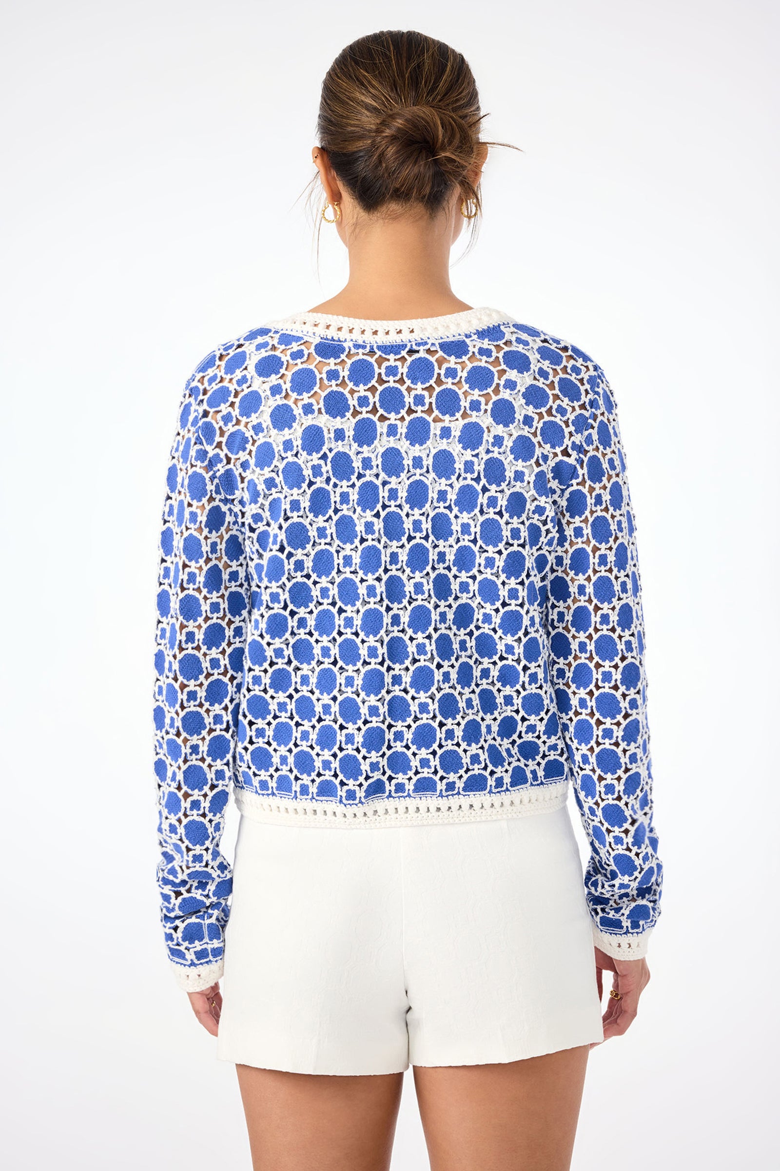 A woman faces away, wearing the Sinai Contrast Trim Knit Cardigan and white shorts. Her hair is in a low bun, set against a plain white background.