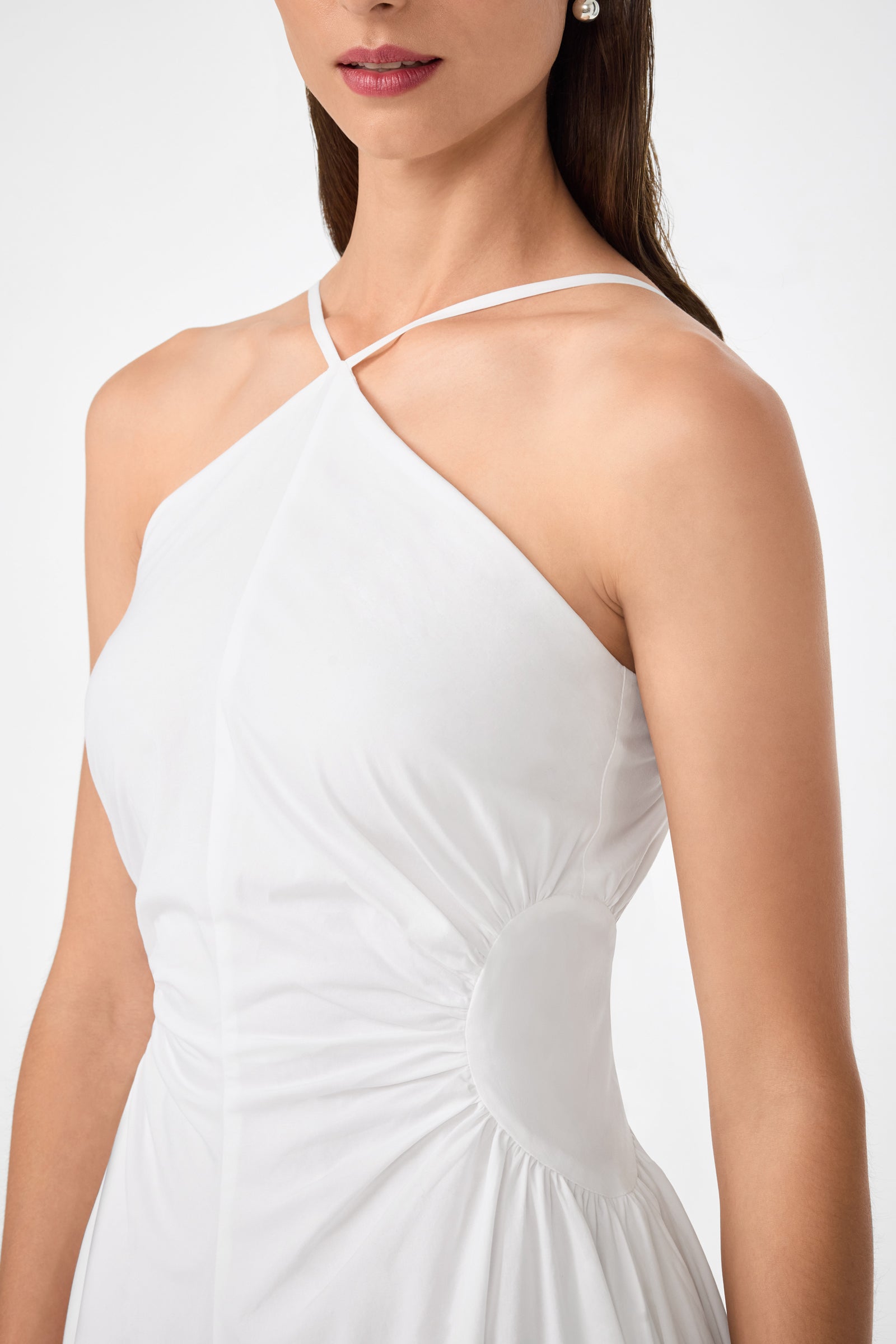 A woman wears the Kata Shirred Waist Midi Dress, a sleeveless white style featuring a crisscross halter neckline and gathered waist detail, shown from shoulders to waist.