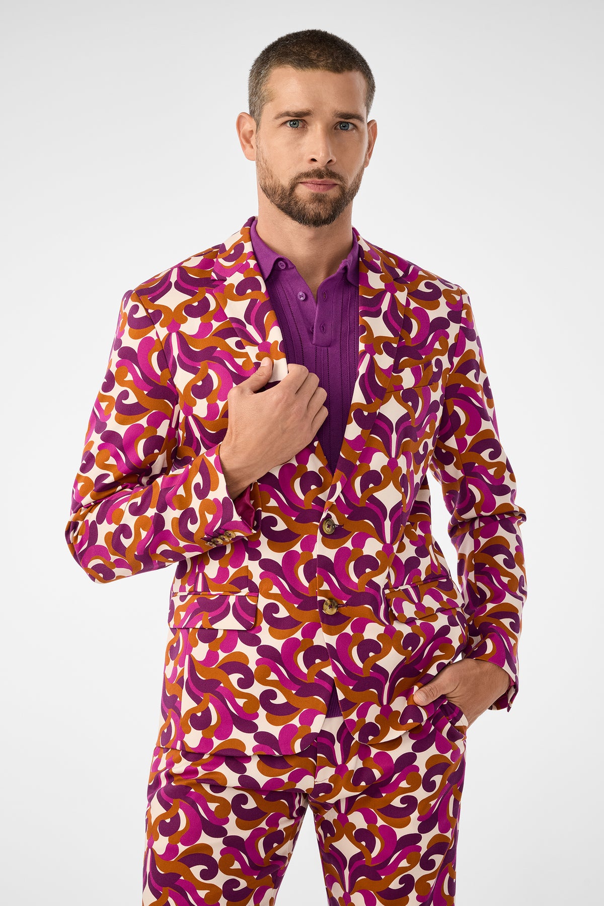A man with short hair and a beard models the Thurston Blazer, featuring a bold swirl of purple, orange, and white over a purple shirt, posing with one hand in his pocket against a plain white background.