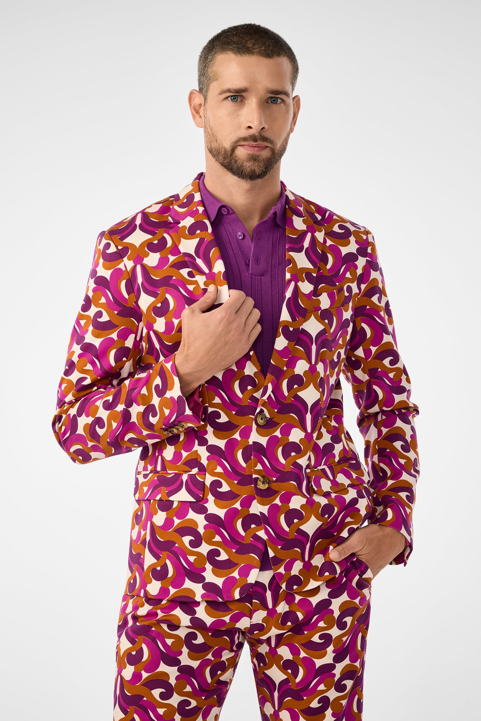A man with short hair and a beard models the Thurston Blazer, featuring a bold swirl of purple, orange, and white over a purple shirt, posing with one hand in his pocket against a plain white background.