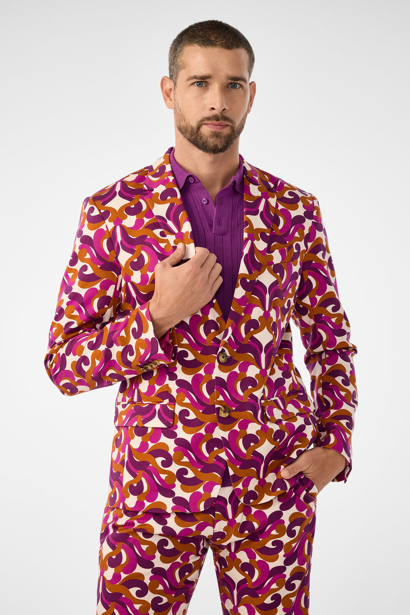 A man with short hair and a beard models the Thurston Blazer, featuring a bold swirl of purple, orange, and white over a purple shirt, posing with one hand in his pocket against a plain white background.