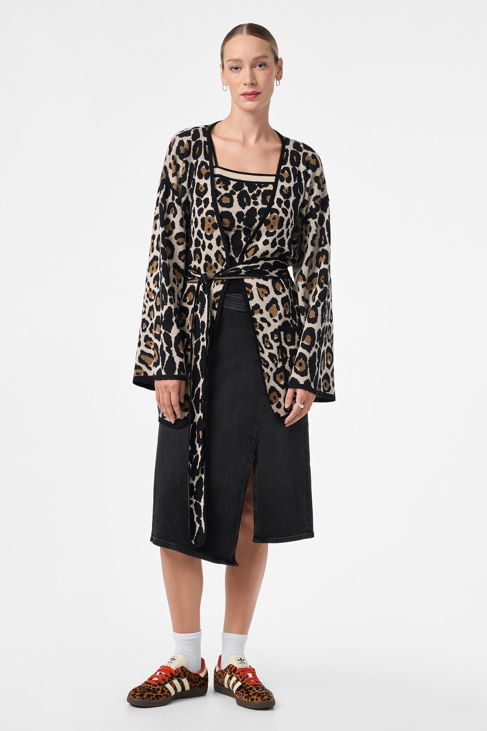 A woman stands facing forward, wearing the Casady Cami with a leopard print cardigan, black knee-length slit skirt, white socks, and leopard print sneakers. Her hair is pulled back and she has hoop earrings.