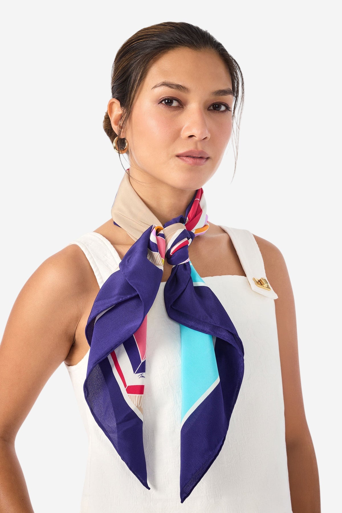 A woman stands confidently against a plain light background, wearing a white sleeveless top and the Umbrella Scarf - Parapluie Silk tied around her neck.