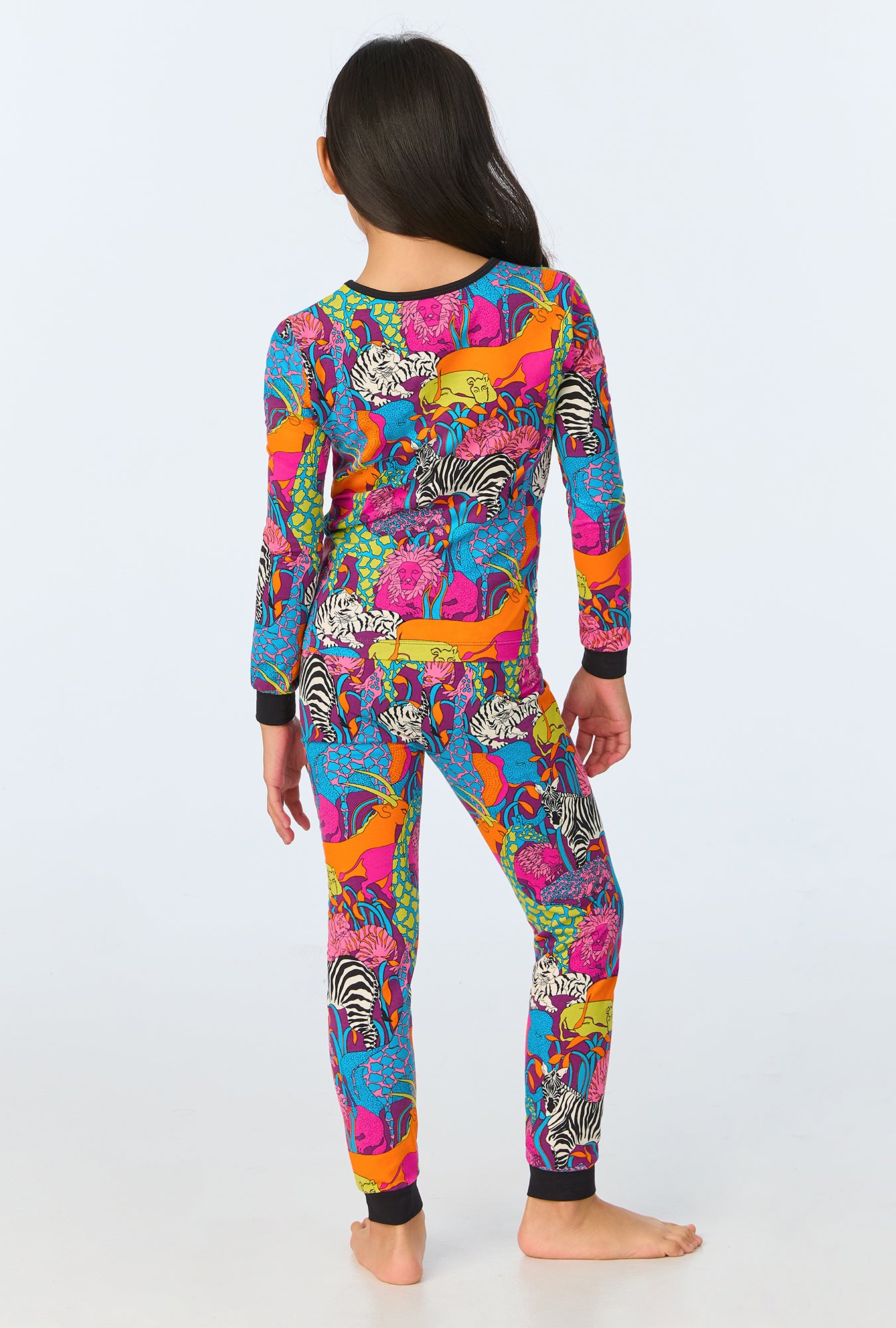 A barefoot child faces away in the Jungle Kids Long-Sleeve Long Pant Jersey PJ Set, featuring vibrant animal prints on blue. These unisex, fitted organic cotton pajamas with black cuffs offer cozy sleepwear for children.