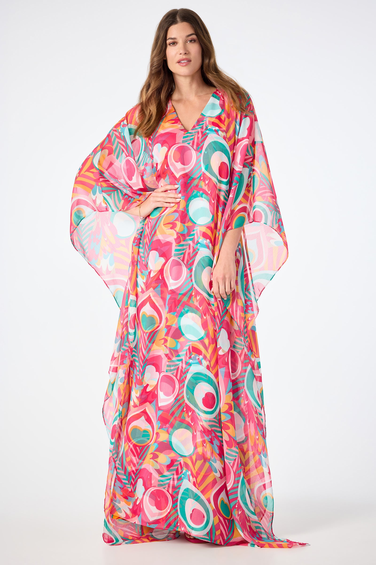 A woman wears the Salon Maxi Caftan Dress in Dramont, featuring vibrant abstract patterns, as she stands against a plain white background.