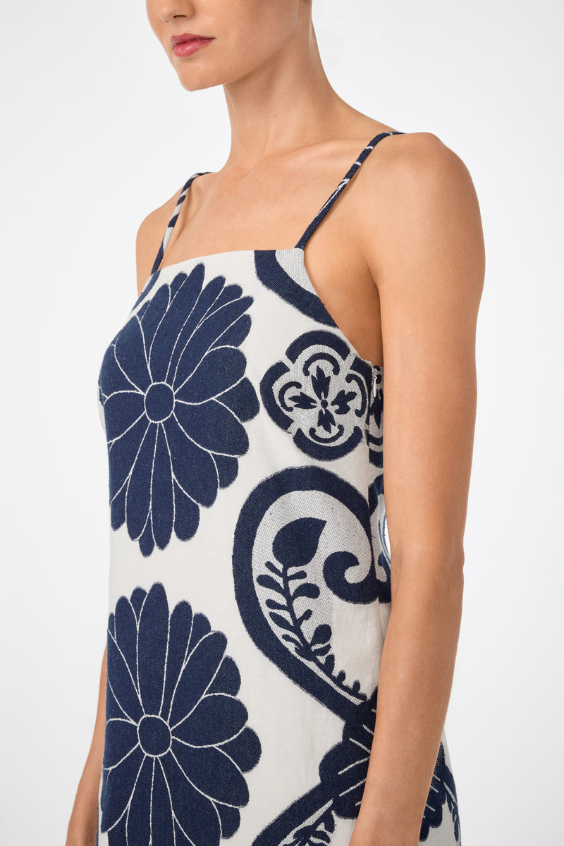 A model wears the Marita 3 Sleeveless Dress, a white dress with thin straps and large navy blue floral patterns, shown from shoulders to mid-thigh against a plain white background.