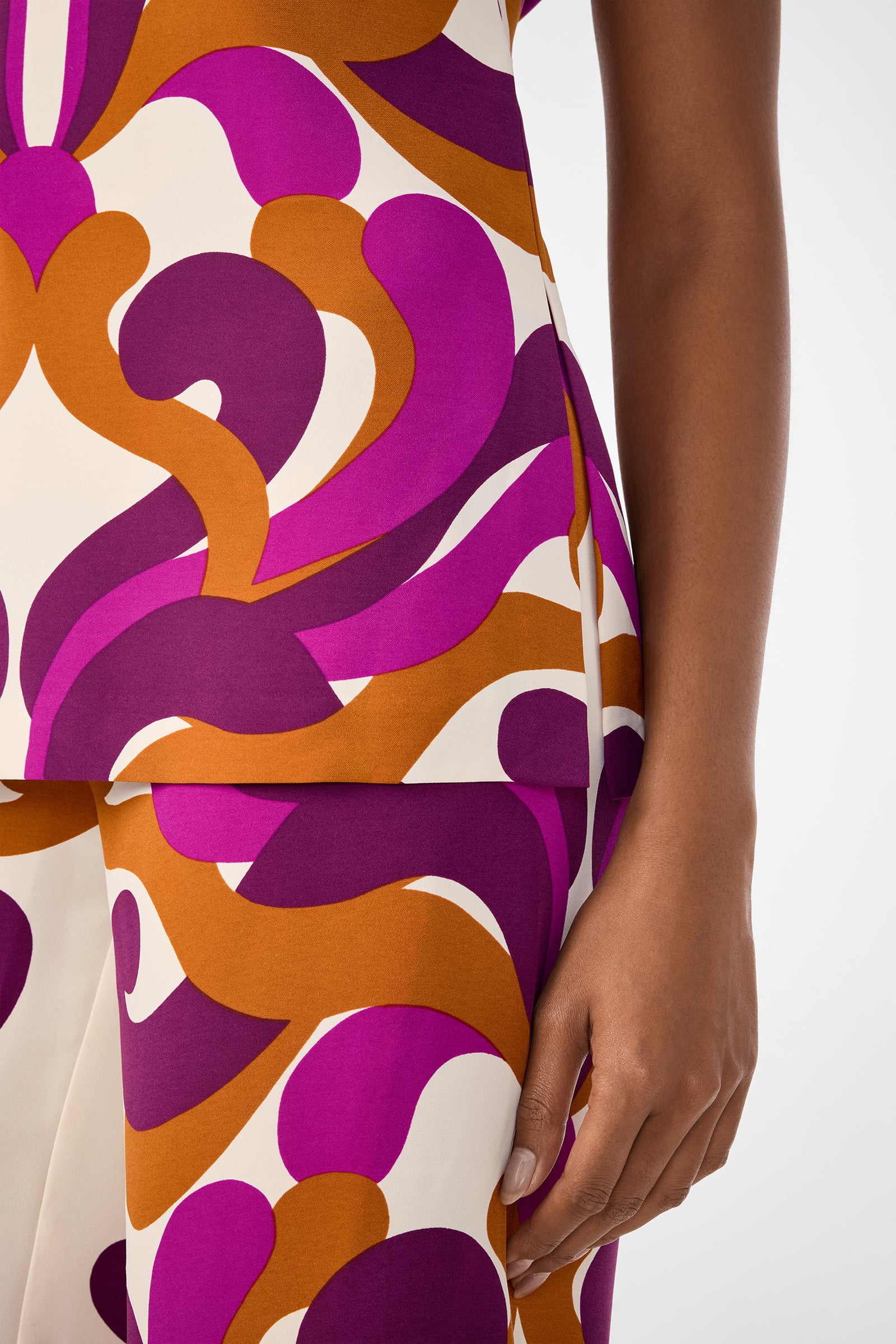 A person wears the Haruto Top, featuring a bold, abstract pattern in purple, orange, and cream, showing their arm and hand against a light background.