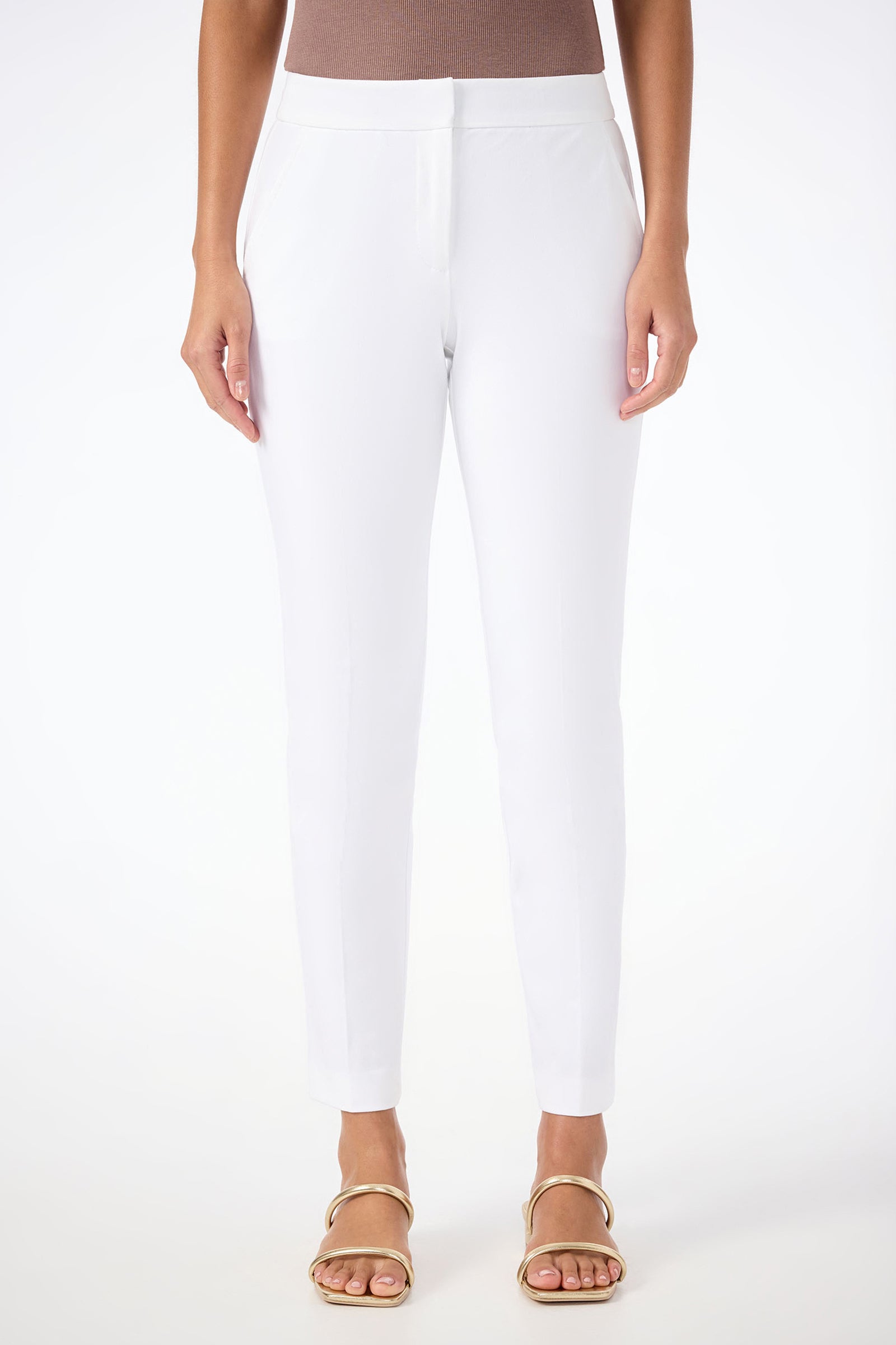 A woman stands against a plain white background wearing Aubree 2 Cigarette Pants in white, a taupe sleeveless top, and gold sandals, with her arms relaxed at her sides.