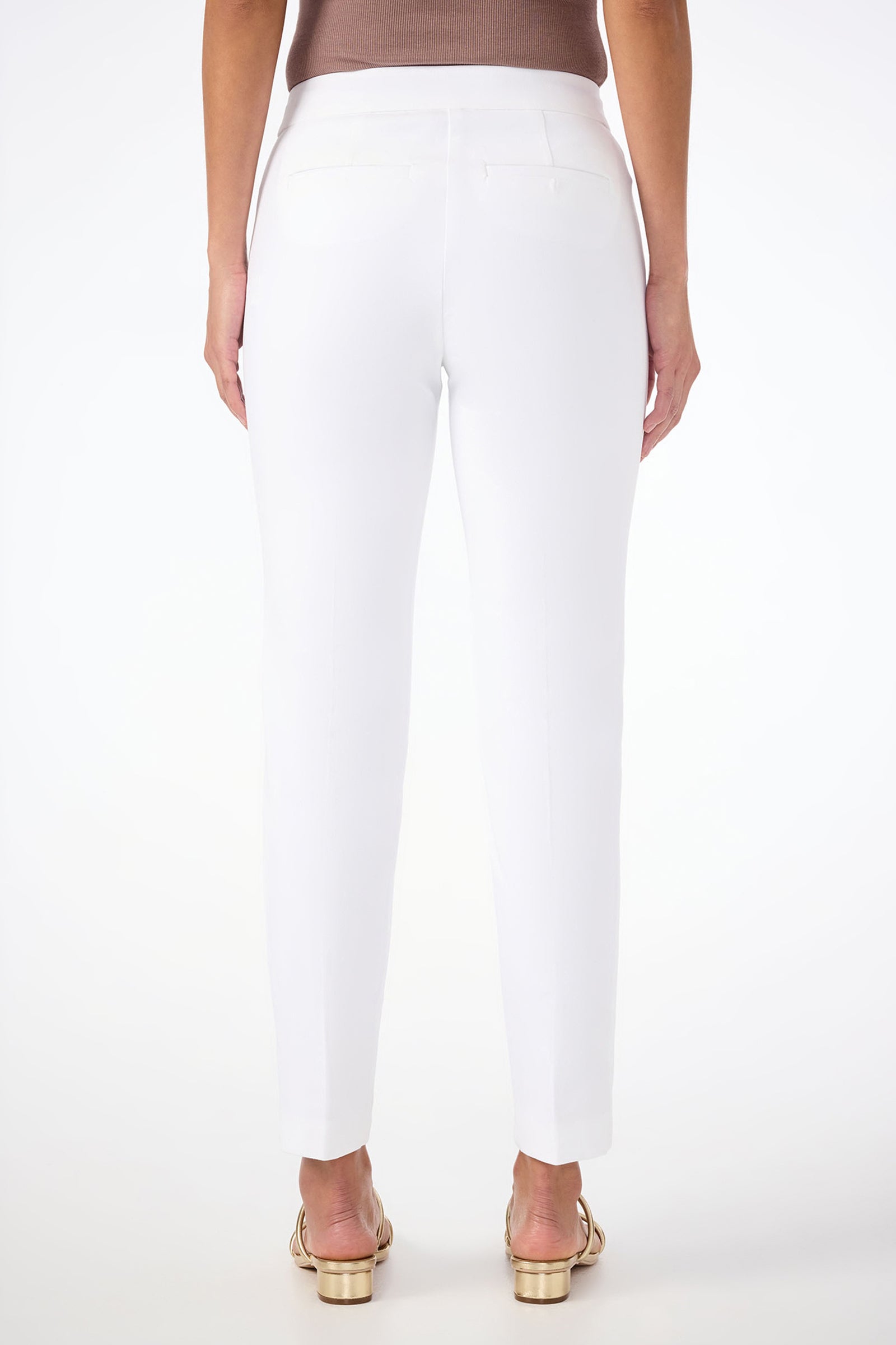 A woman faces away from the camera, wearing Aubree 2 Cigarette Pants in white, a taupe sleeveless top, and gold open-toe sandals against a plain white background.