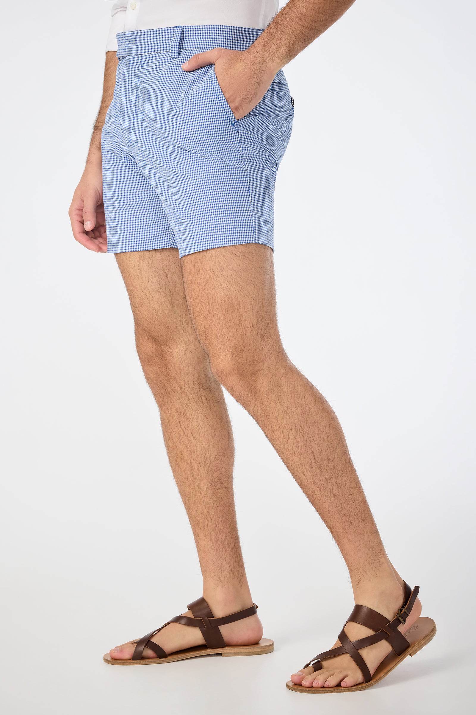 Wearing the Roger Short in Ocean Gingham, a person stands against a plain white background. Only their lower half is visible, paired with a white shirt and brown leather sandals.