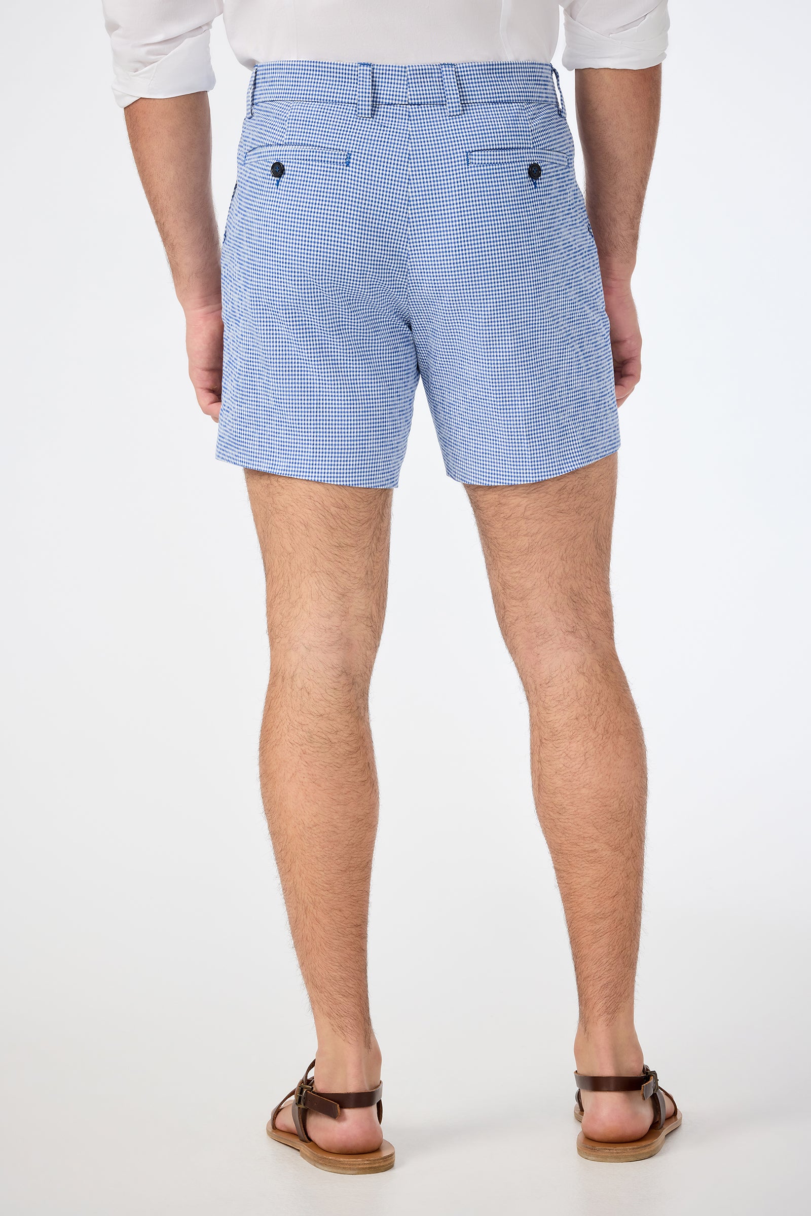 A person stands with their back to the camera, wearing a white shirt and Roger Short - Ocean Gingham blue and white checkered shorts, plus brown sandals, against a plain white background.
