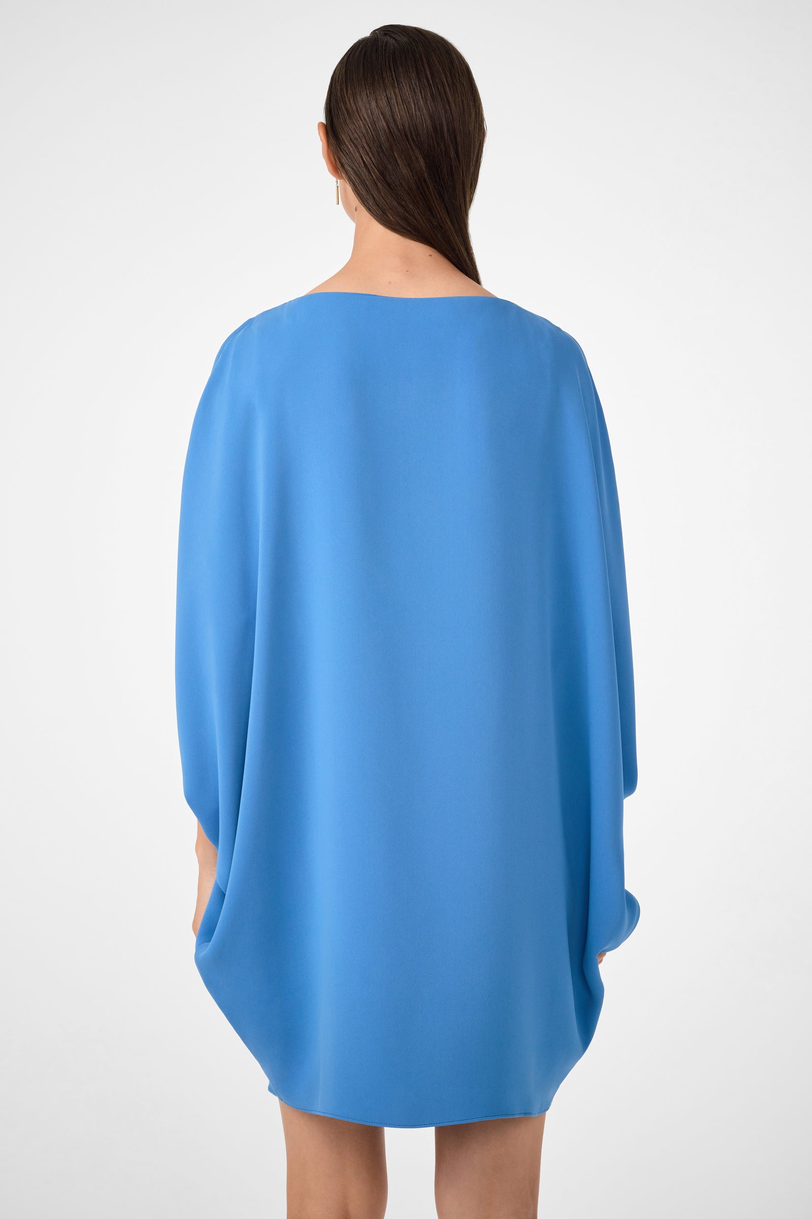 A person with straight brown hair pulled back faces away, wearing the Razu Short Split Sleeve Mini Dress in bright blue. The loose-fitting dress is knee-length with long, flowing split sleeves against a plain white background.