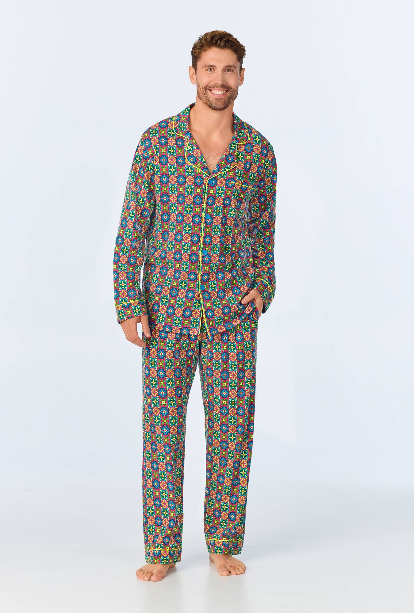 A man stands barefoot, smiling, wearing the Pretty Tiles Mens Long Sleeve Long Pant Jersey PJ Set in Multi against a plain light background.