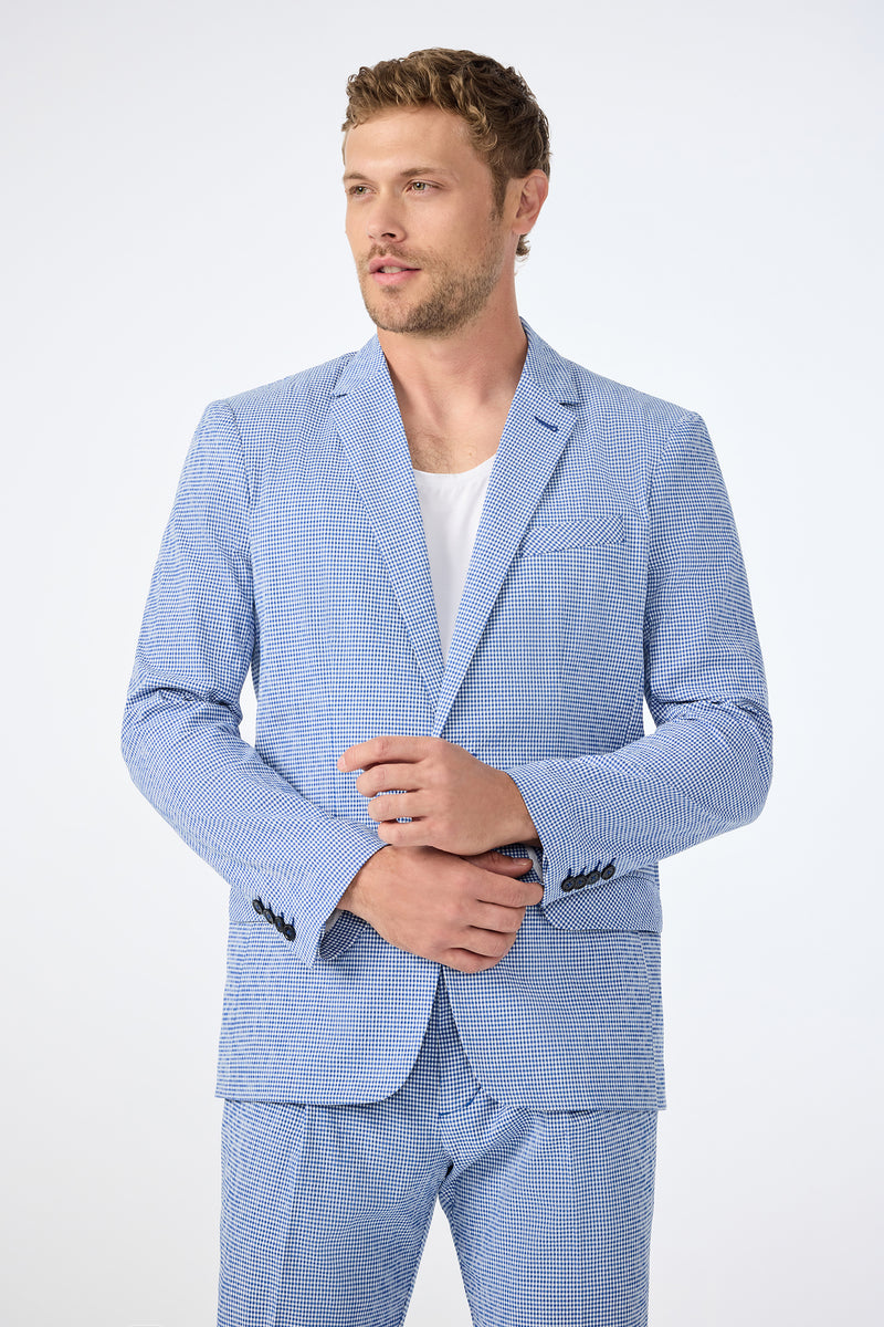 A man wears the Louie Blazer - Ocean Gingham over a white t-shirt, standing against a plain white background and adjusting his sleeve while looking slightly to the side.