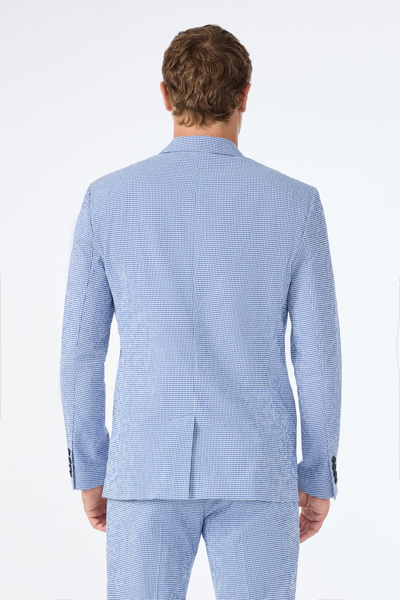 A man is seen from behind wearing the Louie Blazer in Ocean Gingham, featuring a light blue and white checkered pattern, paired with matching trousers against a plain light background.