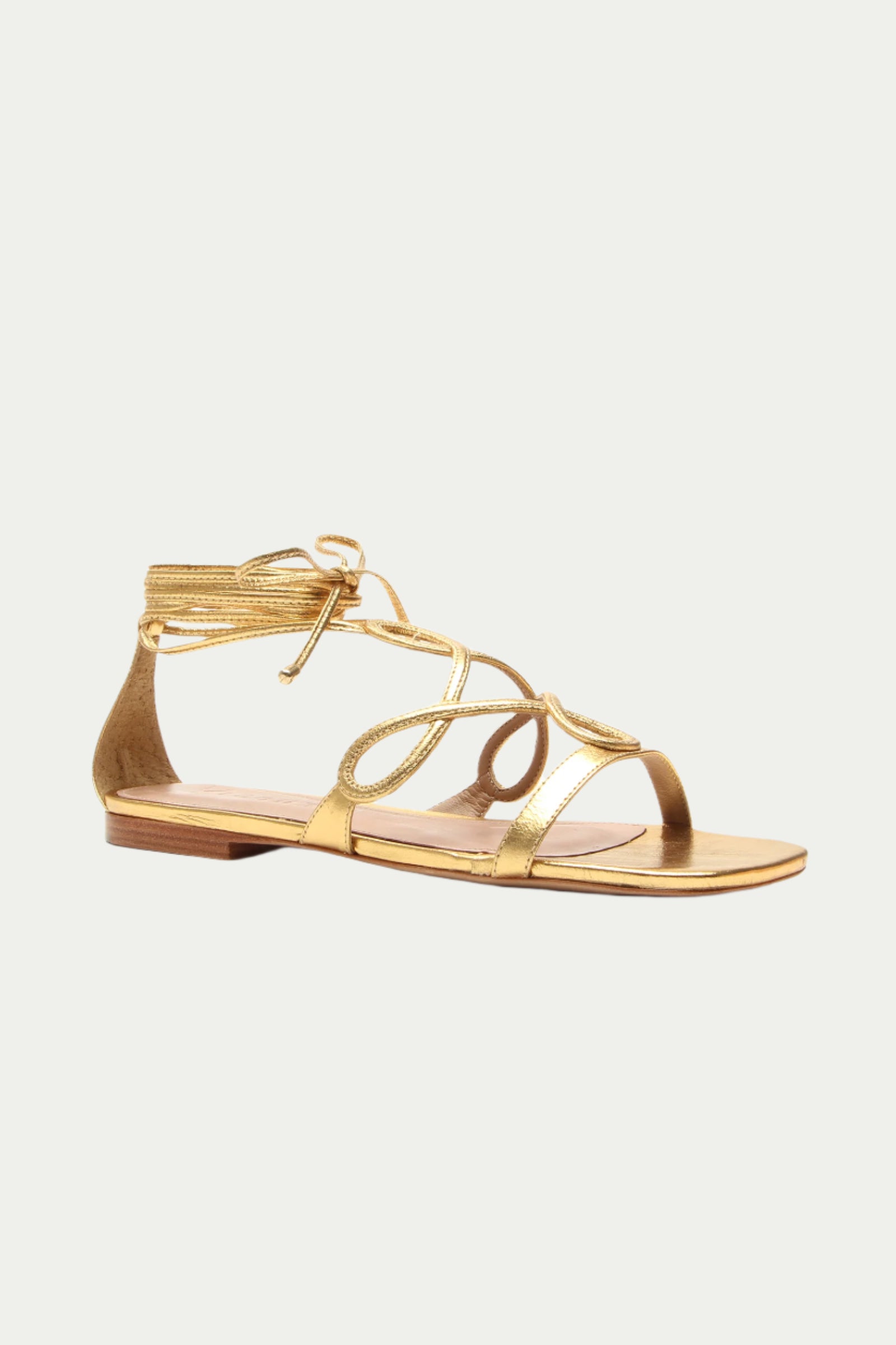 The Gana Strappy Leather Sandal in gold features thin, wrap-around ankle straps, a flat sole, and an open toe design, shown on a plain white background.