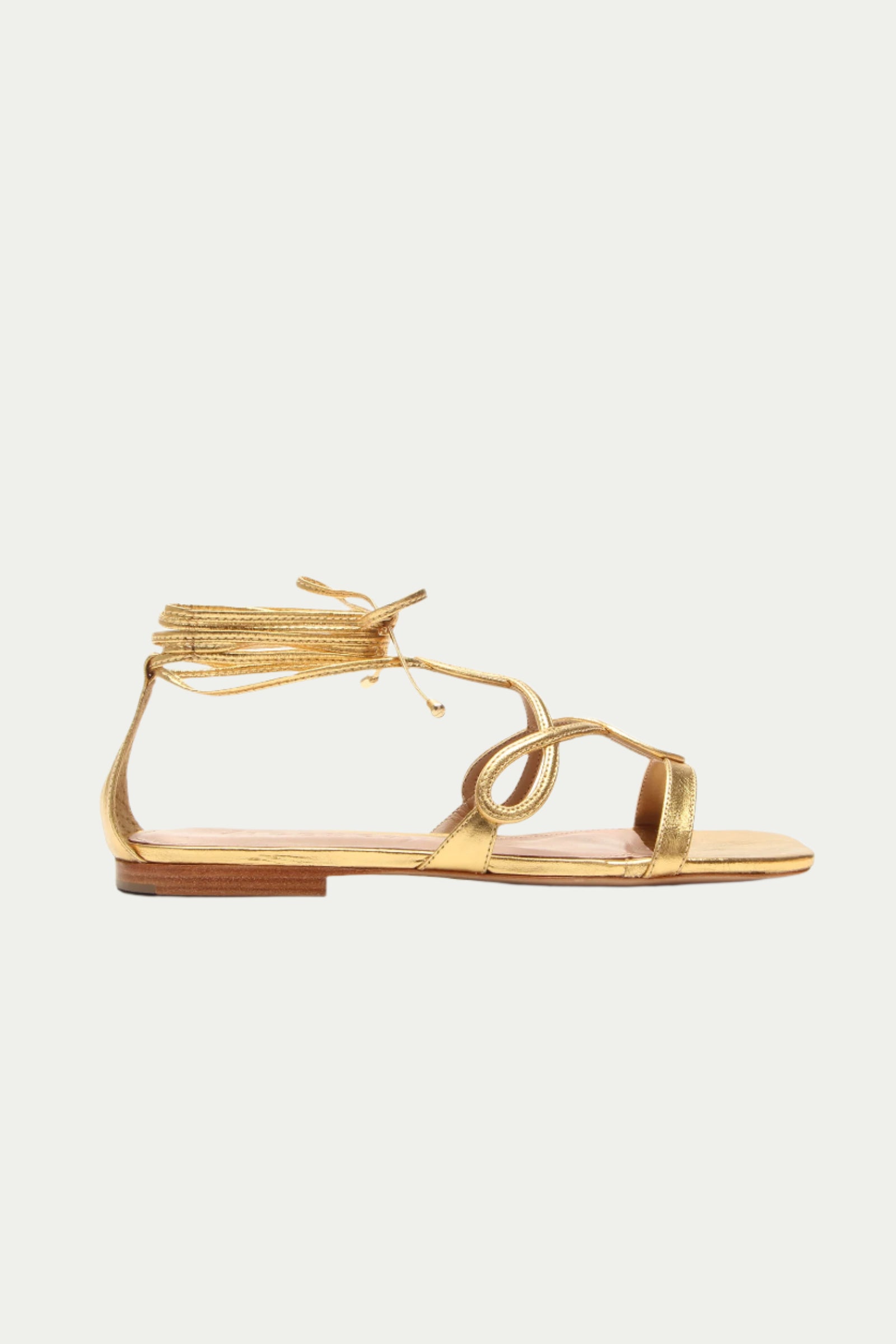 The Gana Strappy Leather Sandal in gold features ankle wrap laces and an open toe, displayed in a side profile on a plain white background.