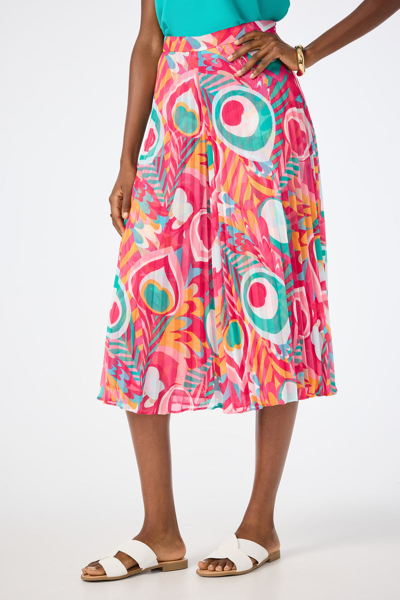 A woman wears Vitrolles Wide-Leg Crop Pants in Dramont, featuring a bold abstract print in pink, teal, yellow, and white. She pairs them with a turquoise top, white sandals, and a gold bracelet. Her hand rests on her hip.