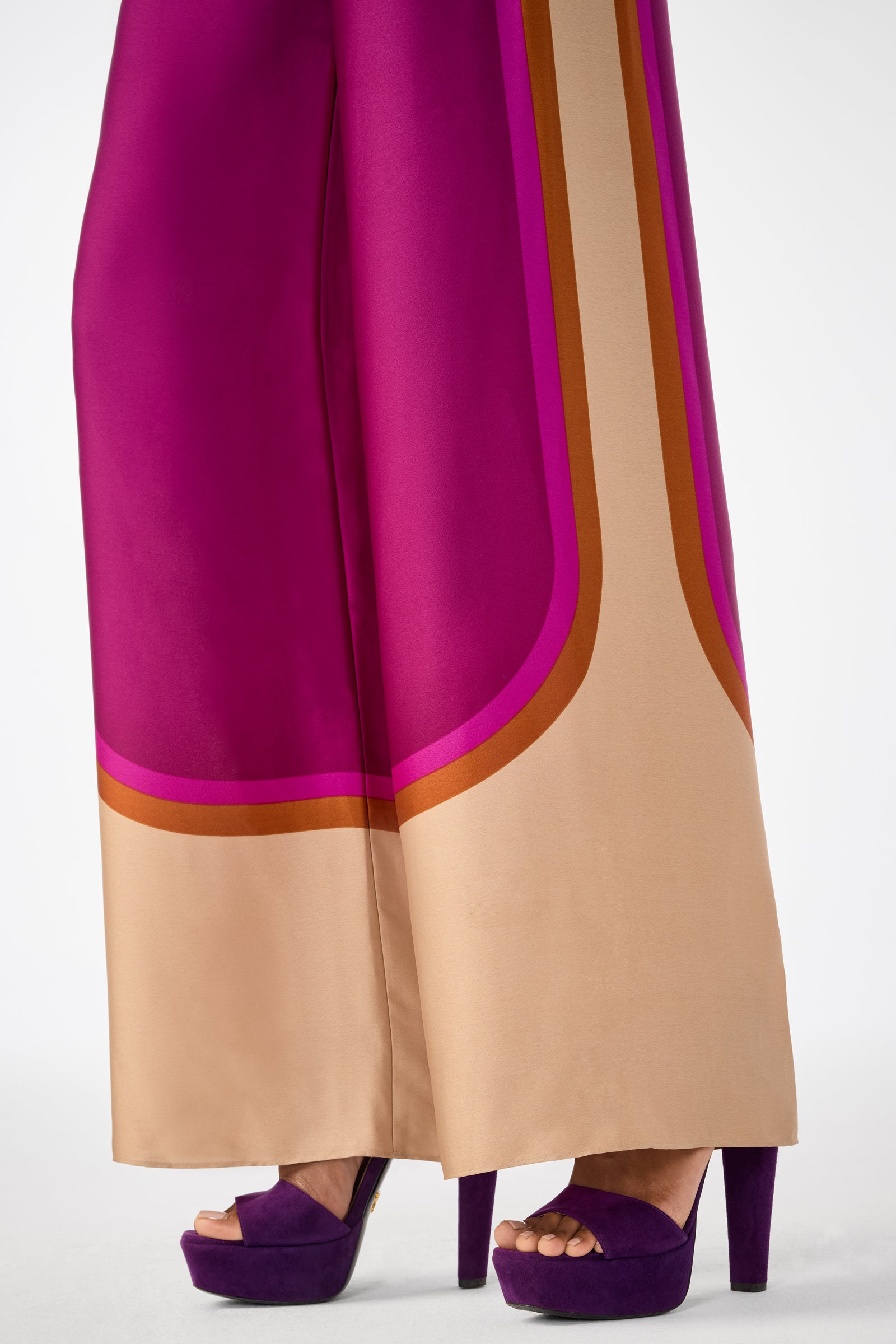 Wearing the Verity 2 Pant, featuring a bold magenta and beige wide-leg design, paired with purple platform high-heeled sandals, on a white background.