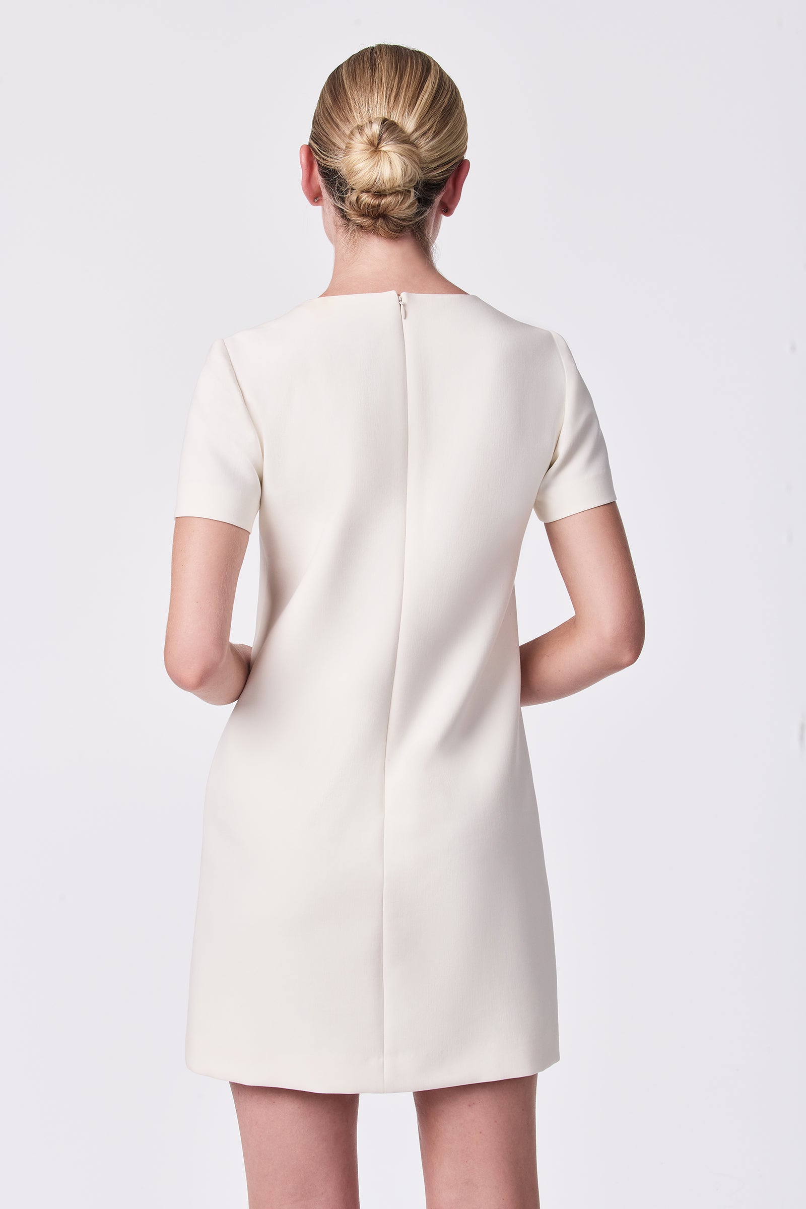 A woman with blonde hair in a neat low bun is shown from the back, wearing the Diamonds Crystal Bows Sheath Dress in Winter White. She stands against a plain white background.