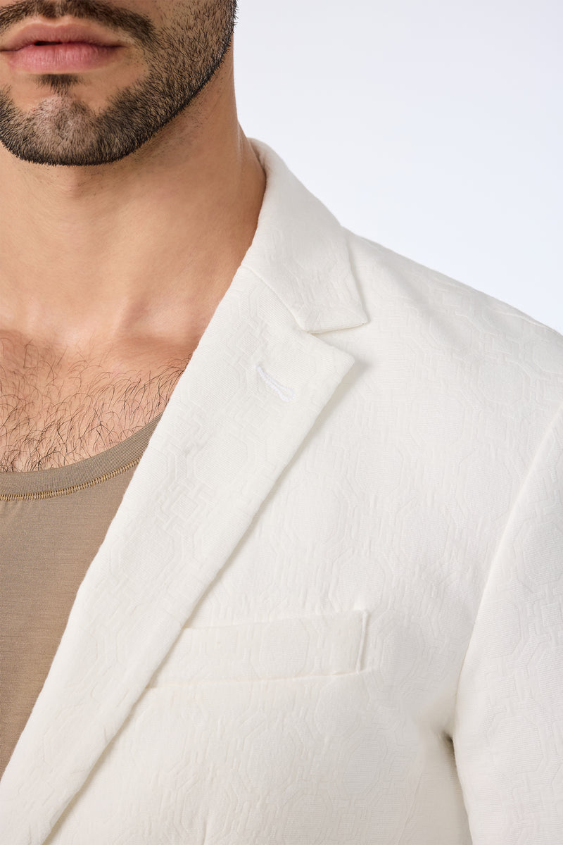 A close-up of a man wearing the Thurston Blazer - Bi-Stretch Cotton in textured white over a beige shirt, with only the lower half of his face, neck, and chest visible against a plain background.
