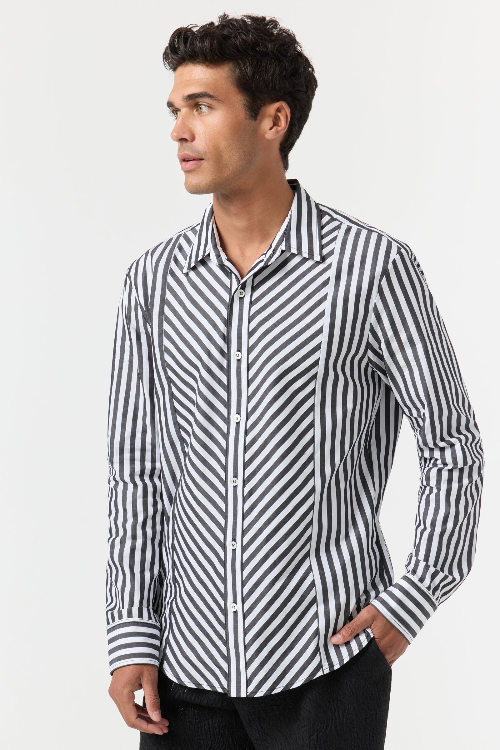A man stands facing left with his right hand in his pocket, wearing the Brody Tux Shirt—a long-sleeve button-up with black and white diagonal and vertical stripes—against a plain white background.