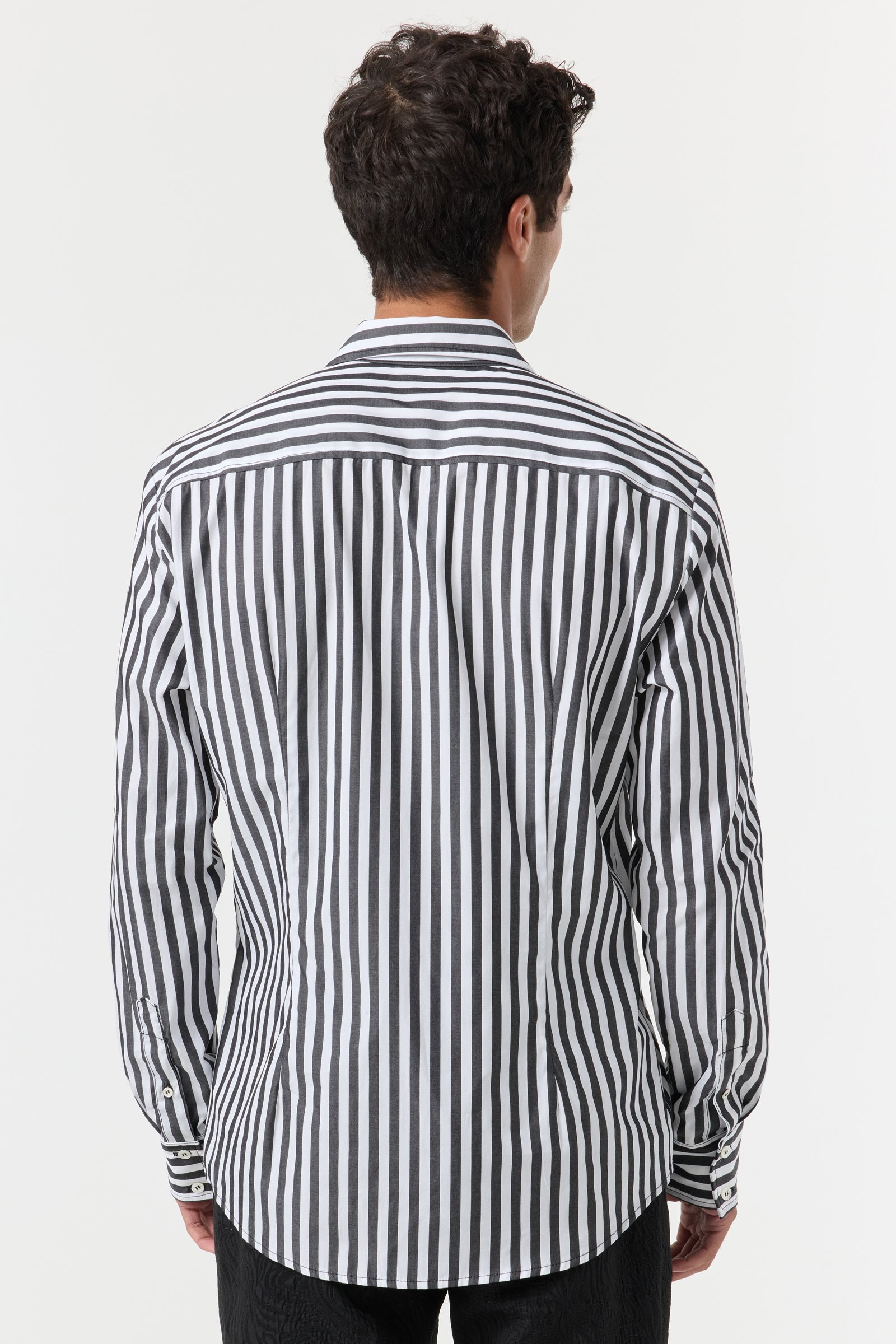 A man with short, dark, curly hair is seen from behind wearing the Brody Tux Shirt, a long-sleeved, button-down shirt with vertical black and white stripes, standing against a plain white background.