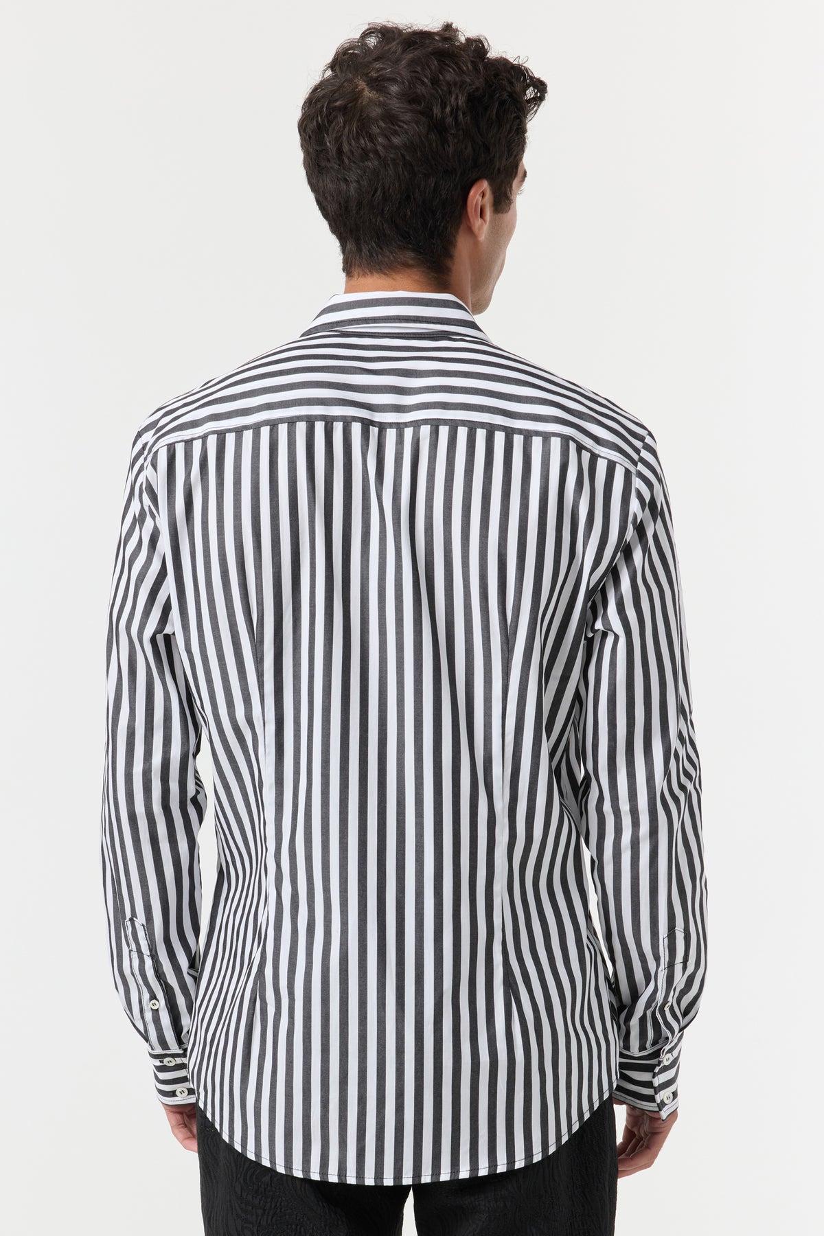 A man with short, dark, curly hair is seen from behind wearing the Brody Tux Shirt, a long-sleeved, button-down shirt with vertical black and white stripes, standing against a plain white background.